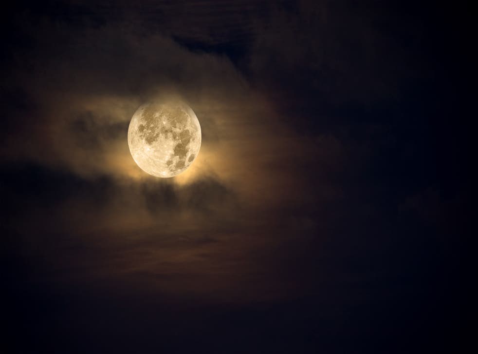 A dark night brings a bright, amber moon alive with puffy hazy clouds.