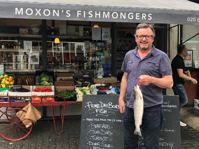 <p>Robin Moxon stands outside one of his fishmongers advertising prime day boat fish</p>