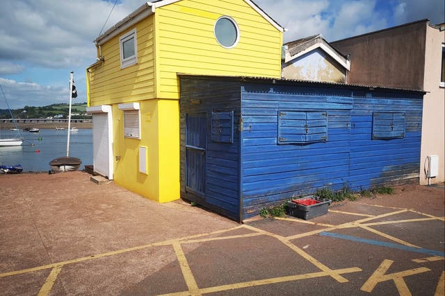 <p>A blue shed attached to a yellow beach hut in Teignmouth, Devon, is up for sale for offers over £45,000</p>