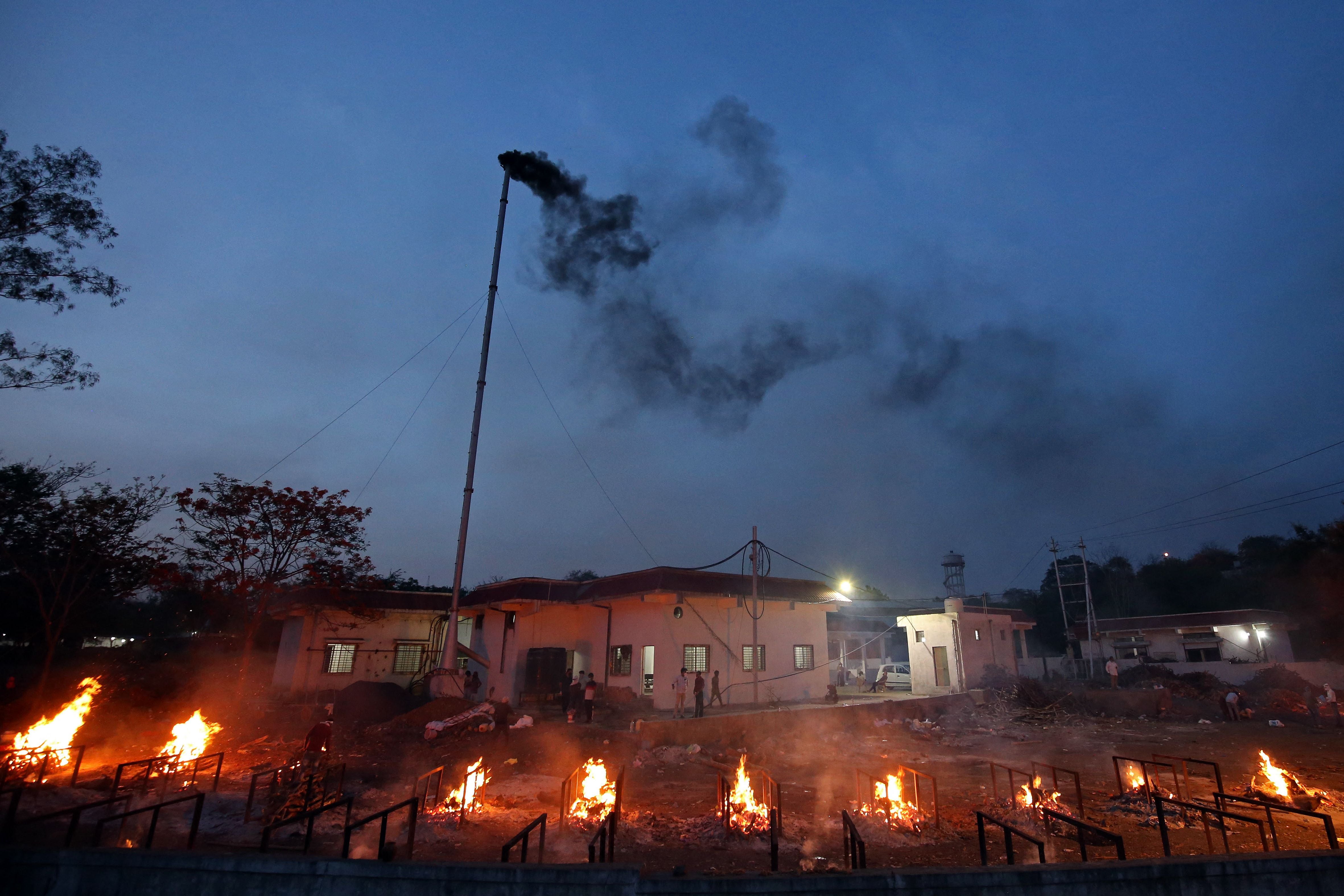 File: Smoke billows from a chimney of an electric crematorium as burning pyres of Covid-19 victims are seen at a crematorium in Bhopal on 23 April, 2021