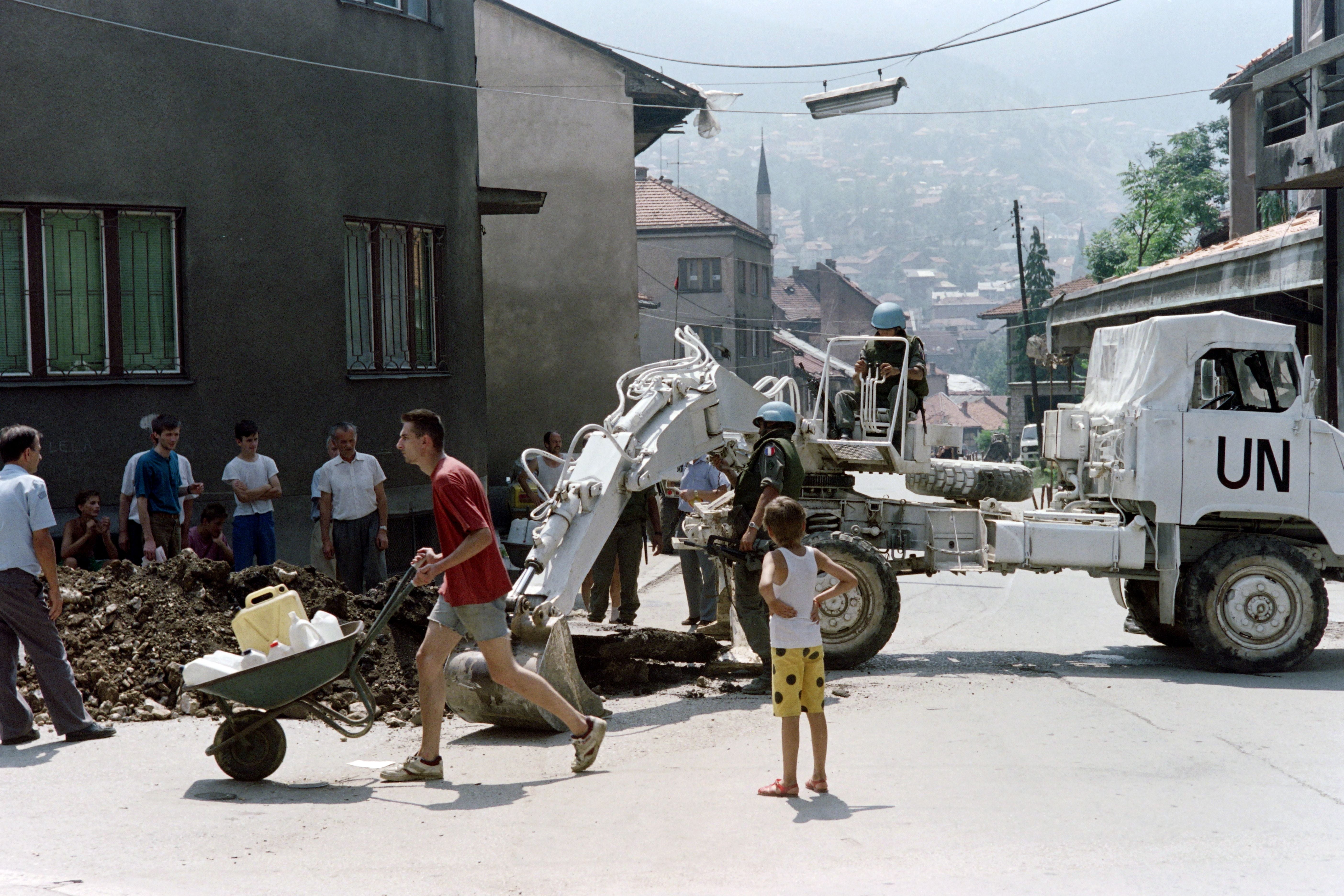 A man carrying jerrycans passes by a UN bulldozer in the streets of Sarajevo during the Bosnian war
