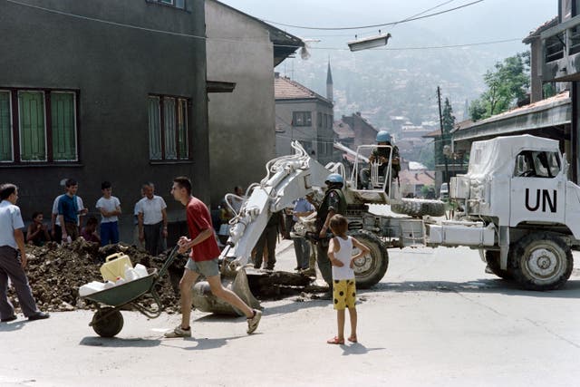 <p>A man carrying jerrycans passes by a UN bulldozer in the streets of Sarajevo during the Bosnian war</p>