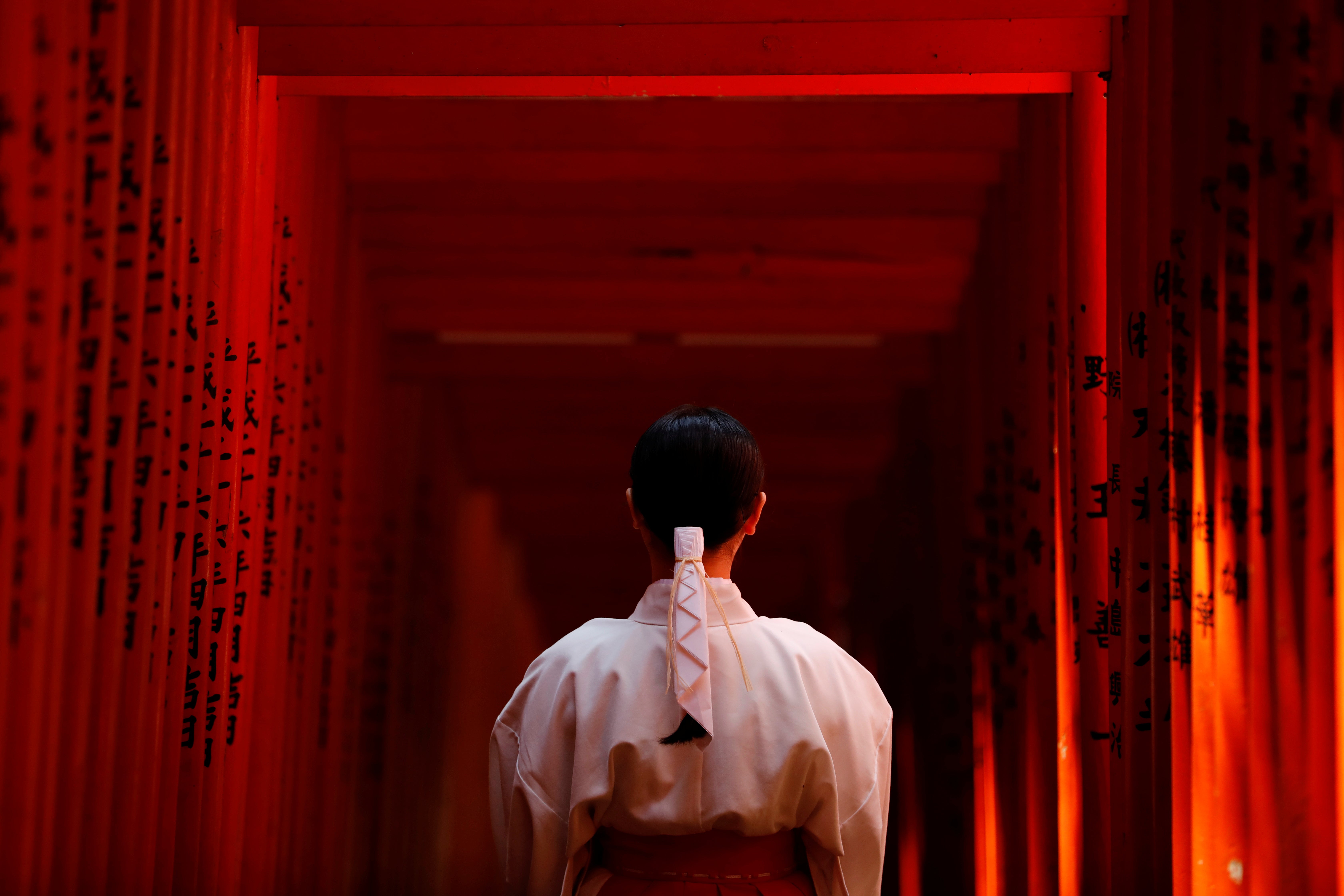 Shouko Totsuka, a Miko also known as a shrine maiden, poses for a photograph as she stands inside the tunnel of Red Torii Gate at the Hie-Jinja Shinto Shrine in Tokyo