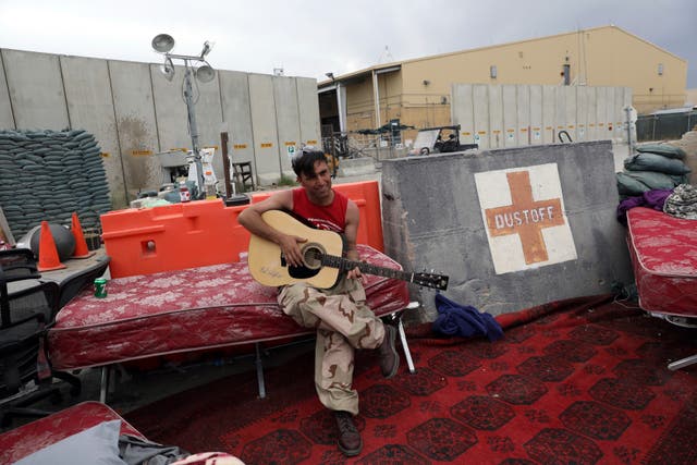 <p>An Afghan soldier plays a guitar that was left behind after the American military departed Bagram air base, in Parwan province north of Kabul.</p>