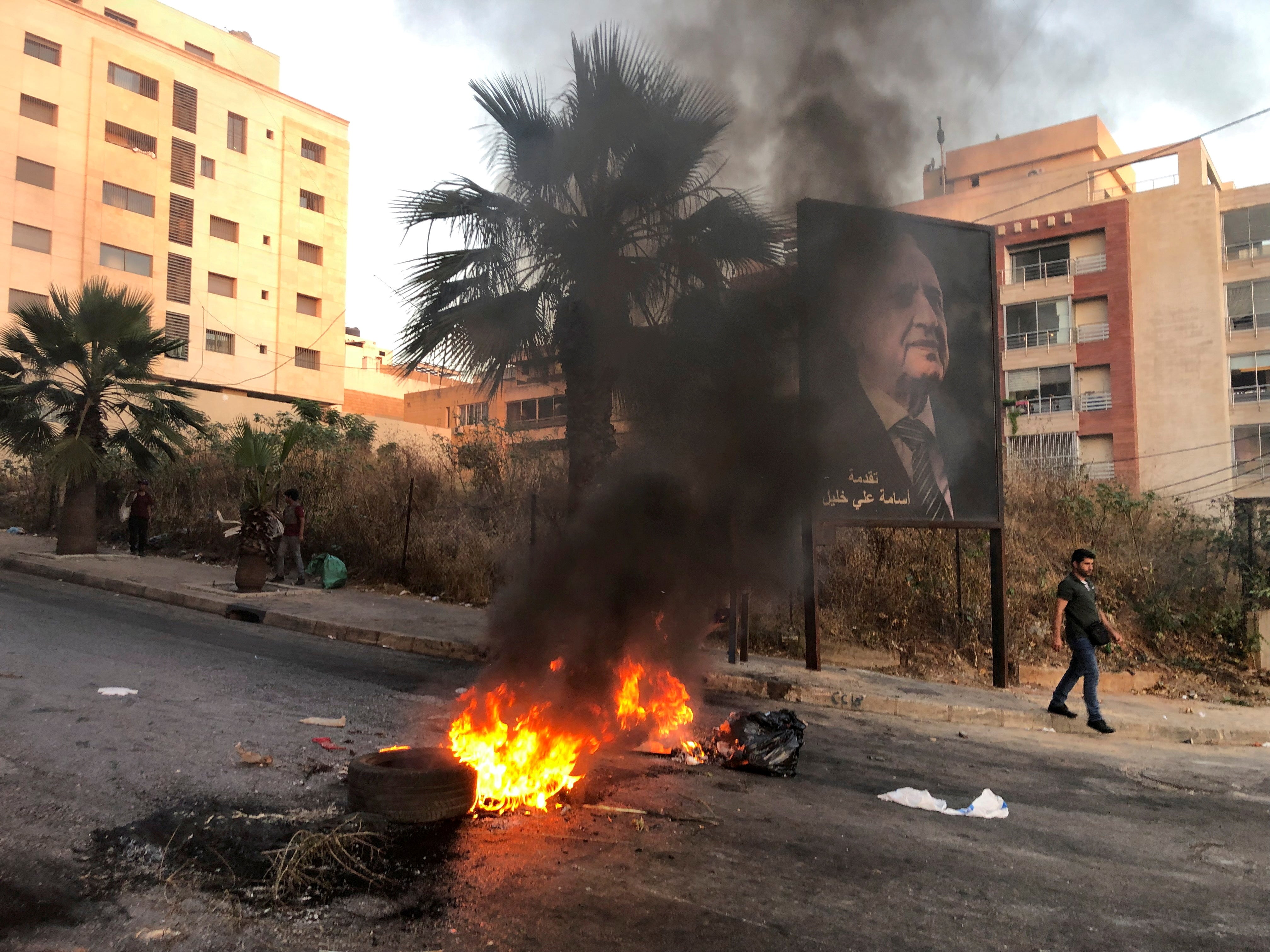 A man walks near a burning fire blocking a road during a protest against mounting economic hardships in Beirut