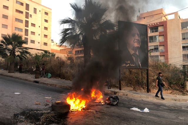 <p>A man walks near a burning fire blocking a road during a protest against mounting economic hardships in Beirut</p>