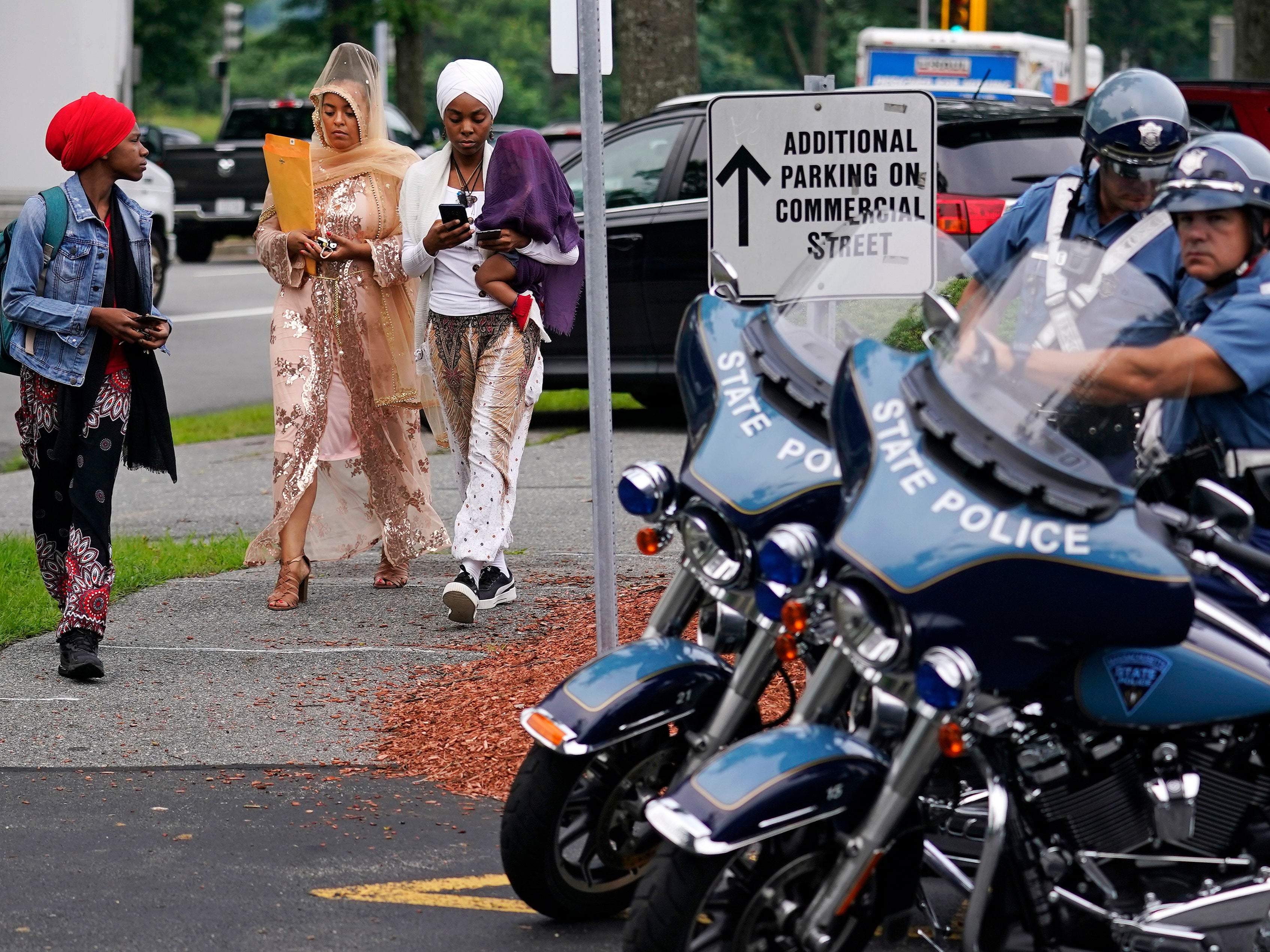 Three women walk past Massachusetts State Police troopers while arriving to sit in the gallery at Malden District Court, following the arrest of several men in an armed standoff on Interstate 95