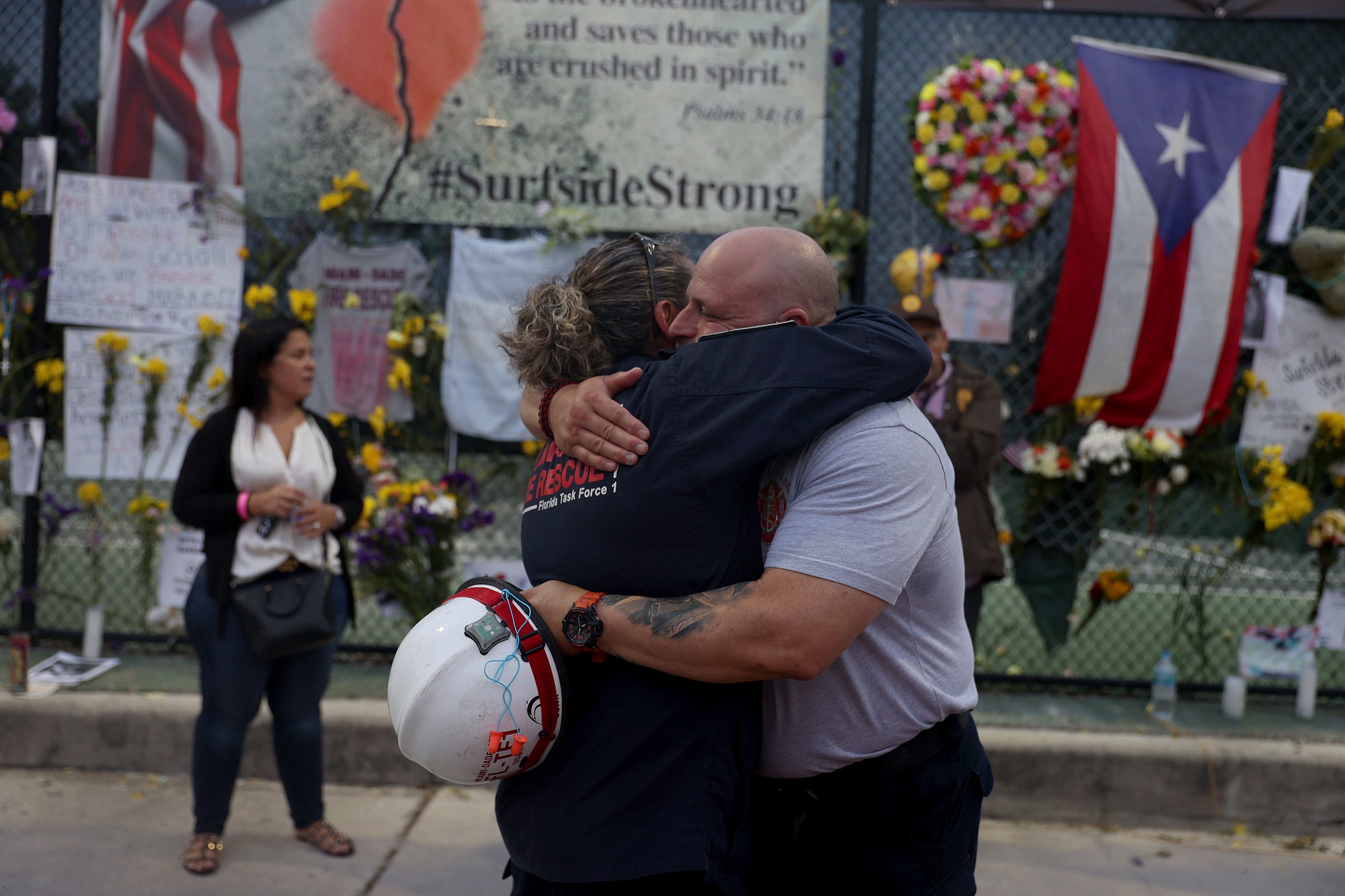 Search and Rescue personnel Maggie Castro (L) and Eddy Alarcon hug as they visit the memorial to the victims in the collapsed 12-story Champlain Towers South condo building as the search and rescue efforts are reported be transitioning to a recovery operation on 7 July, 2021 in Surfside, Florida.