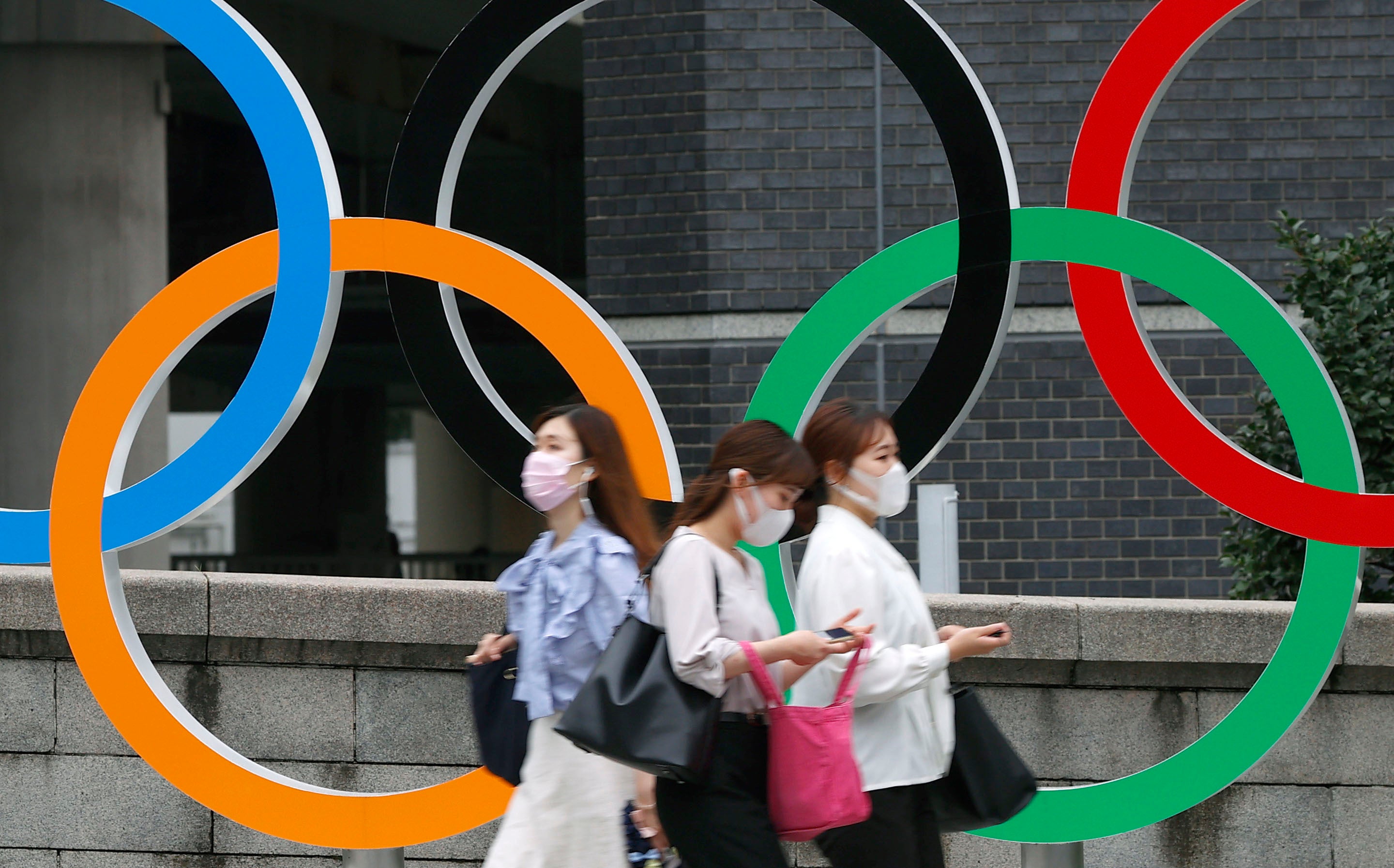 People wearing face masks walk past the Olympics Rings statue in Tokyo on 8 July 2021