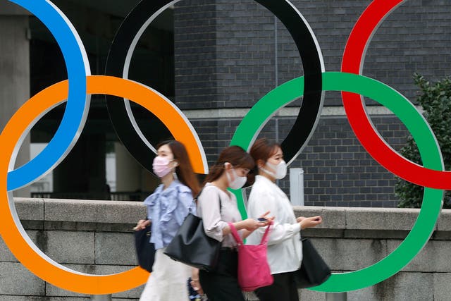 <p>People wearing face masks walk past the Olympics Rings statue in Tokyo on 8 July 2021</p>