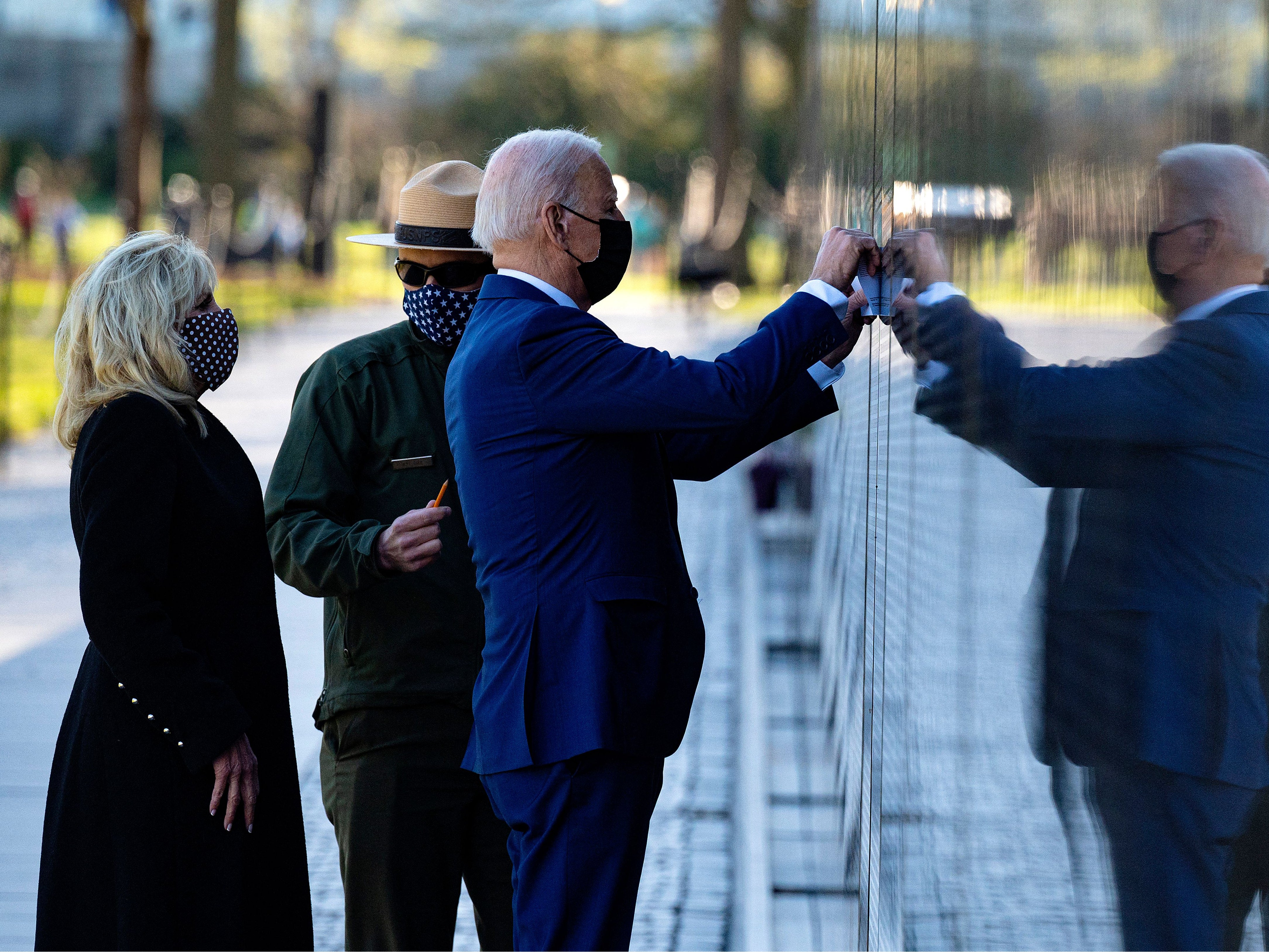 <p>US President Joe Biden, flanked by First Lady Dr Jill Biden, uses paper to trace the name of veteran Dennis F Shine as they visit the Vietnam Veterans Memorial for National Vietnam War Veterans Day in Washington, DC, on March 29, 2021</p>