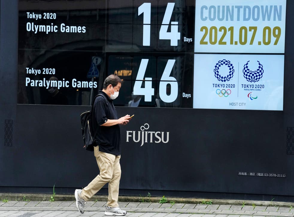 A man wearing a face mask walks past the countdown clock for the Tokyo Olympic and Paralympic Games near Shimbashi station