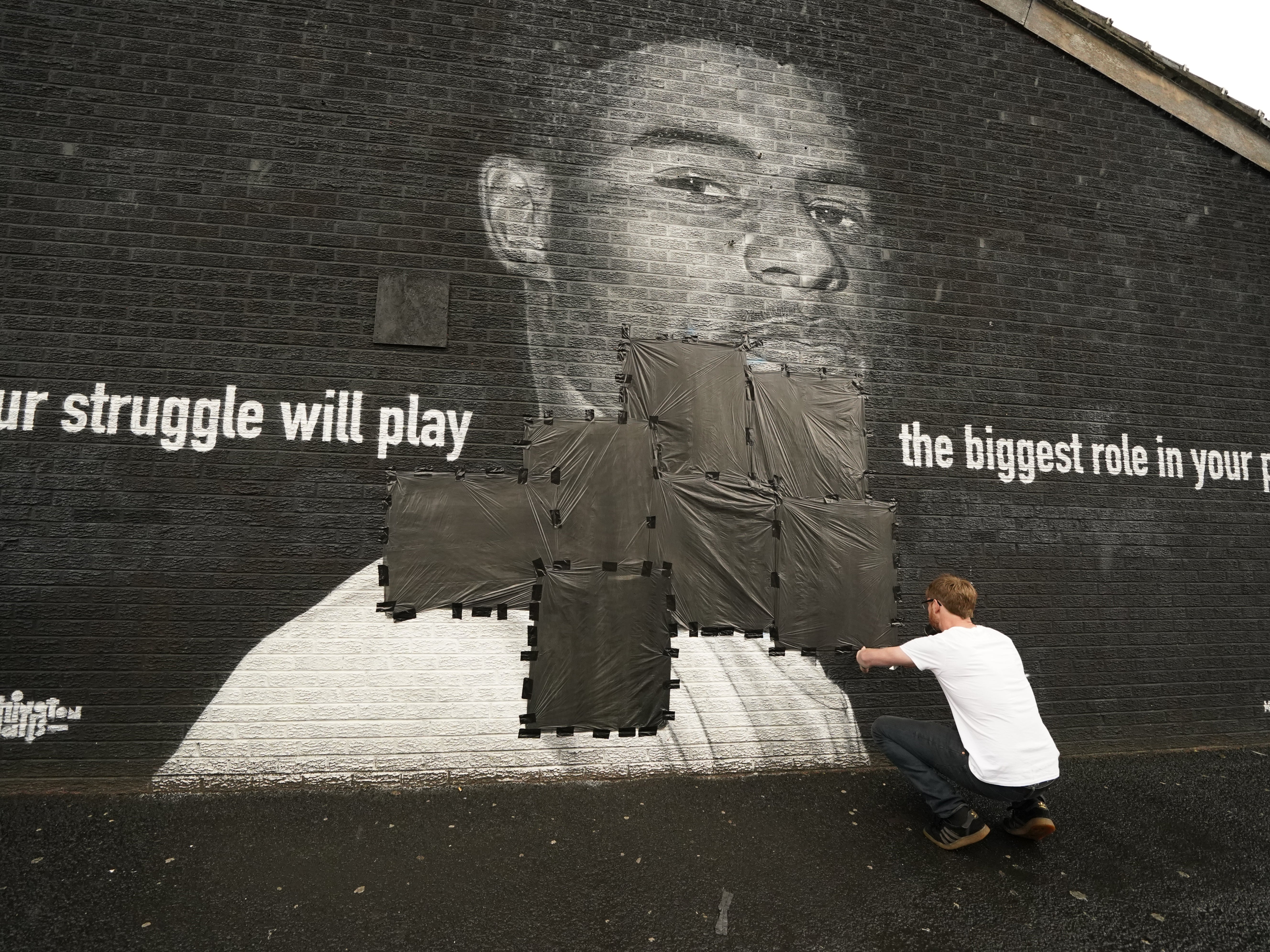 Local resident Ed Wellard tapes bin liners over graffiti on the mural of Marcus Rashford in Copson Street, Withington.