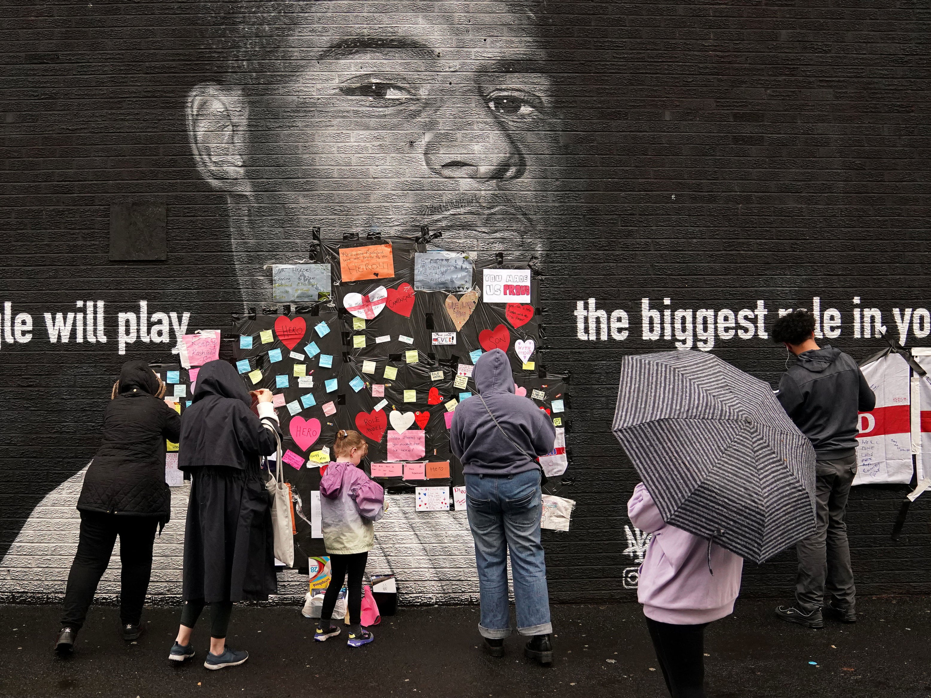 People place messages of support on top of bin liners that were placed over offensive wording on the mural of Manchester United striker and England player Marcus Rashford