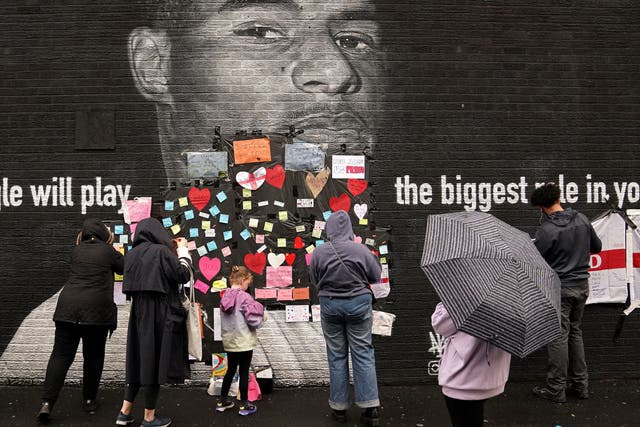 <p>People place messages of support on top of bin liners that were placed over offensive wording on the mural of Manchester United striker and England player Marcus Rashford</p>
