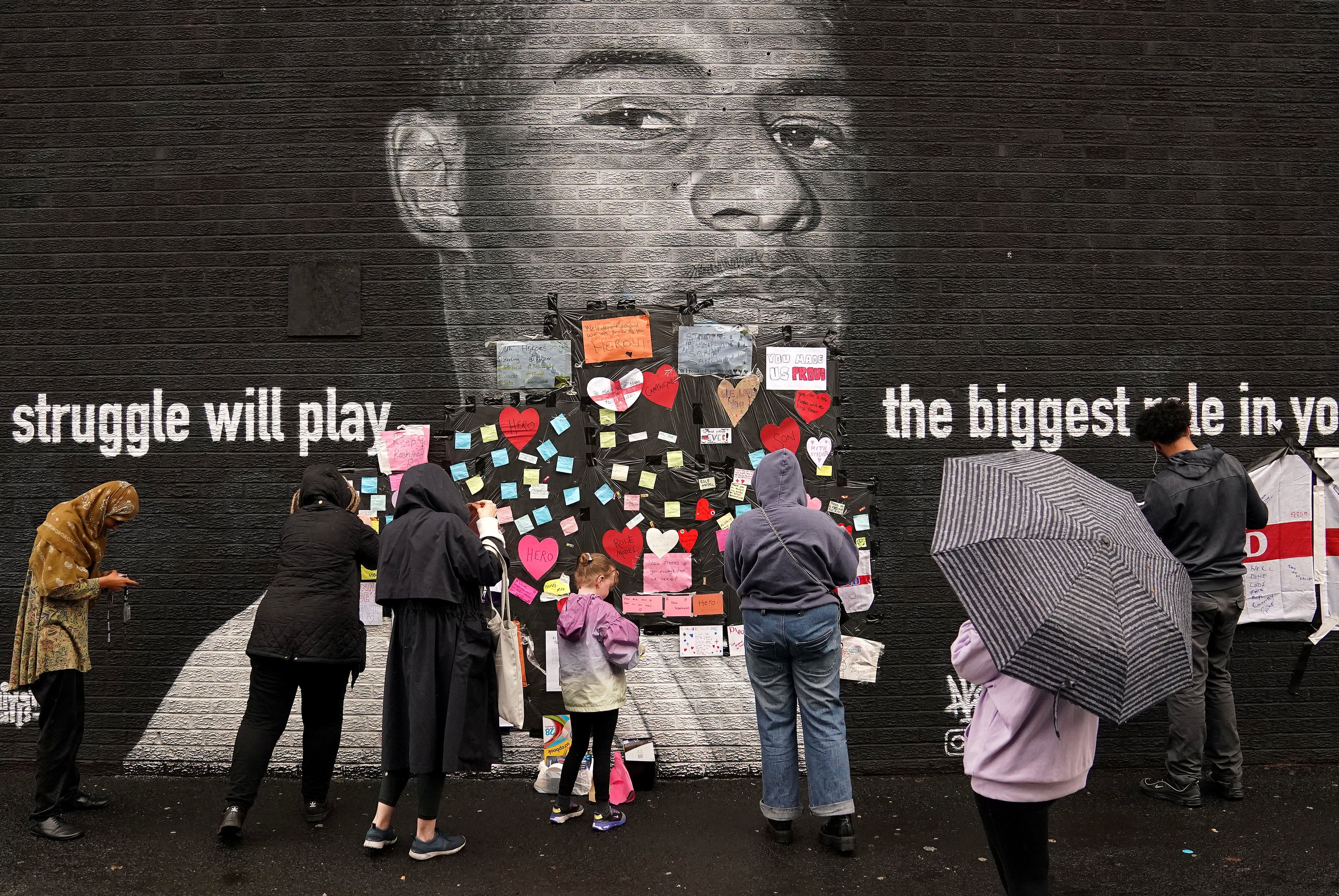 People place messages of support on top of bin liners that were placed over offensive wording on the mural of Manchester United striker and England player Marcus Rashford on the wall of the Coffee House Cafe on Copson Street, Withington