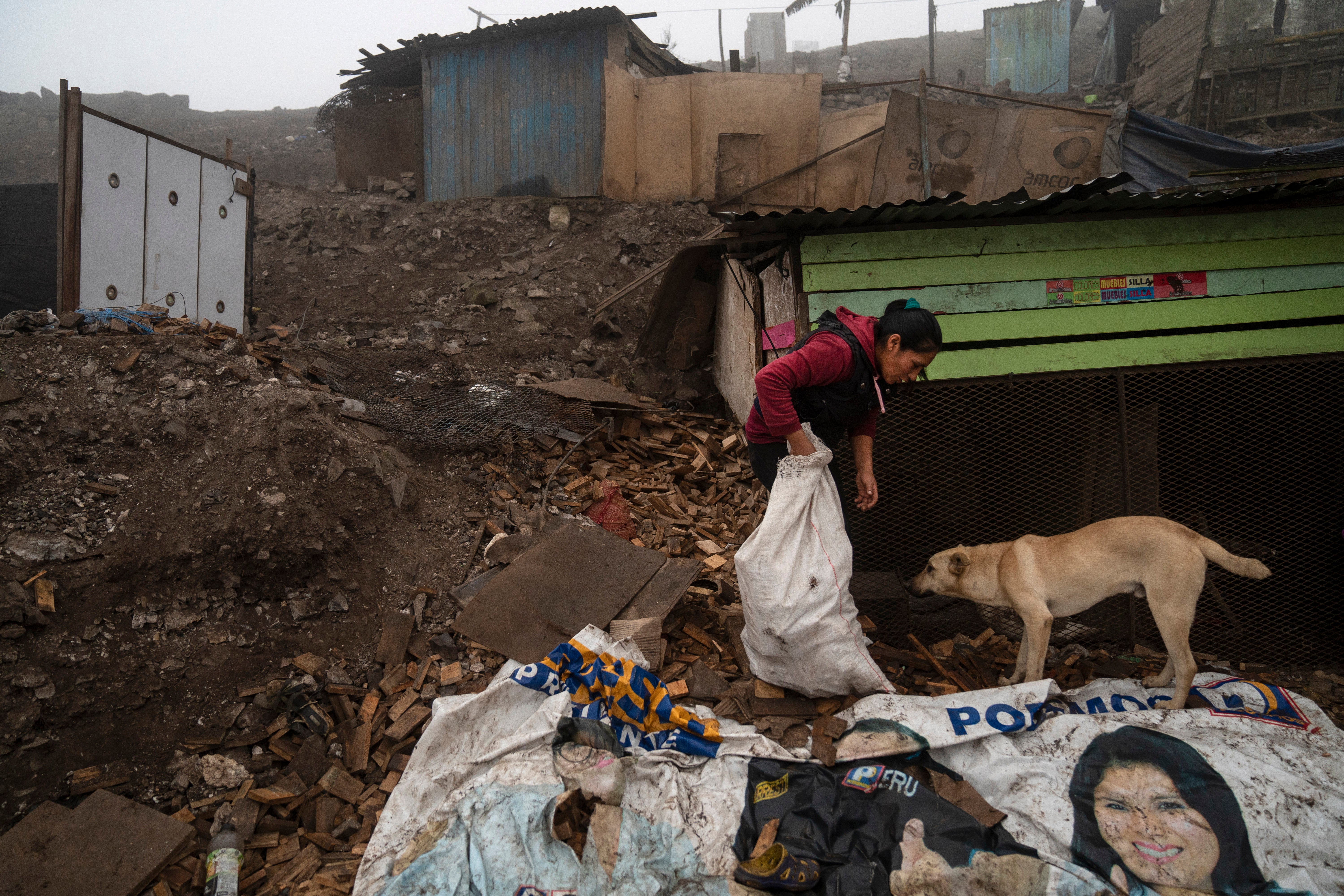 A woman gathers wood near a discarded campaign poster in the Lima slum of Goshen City
