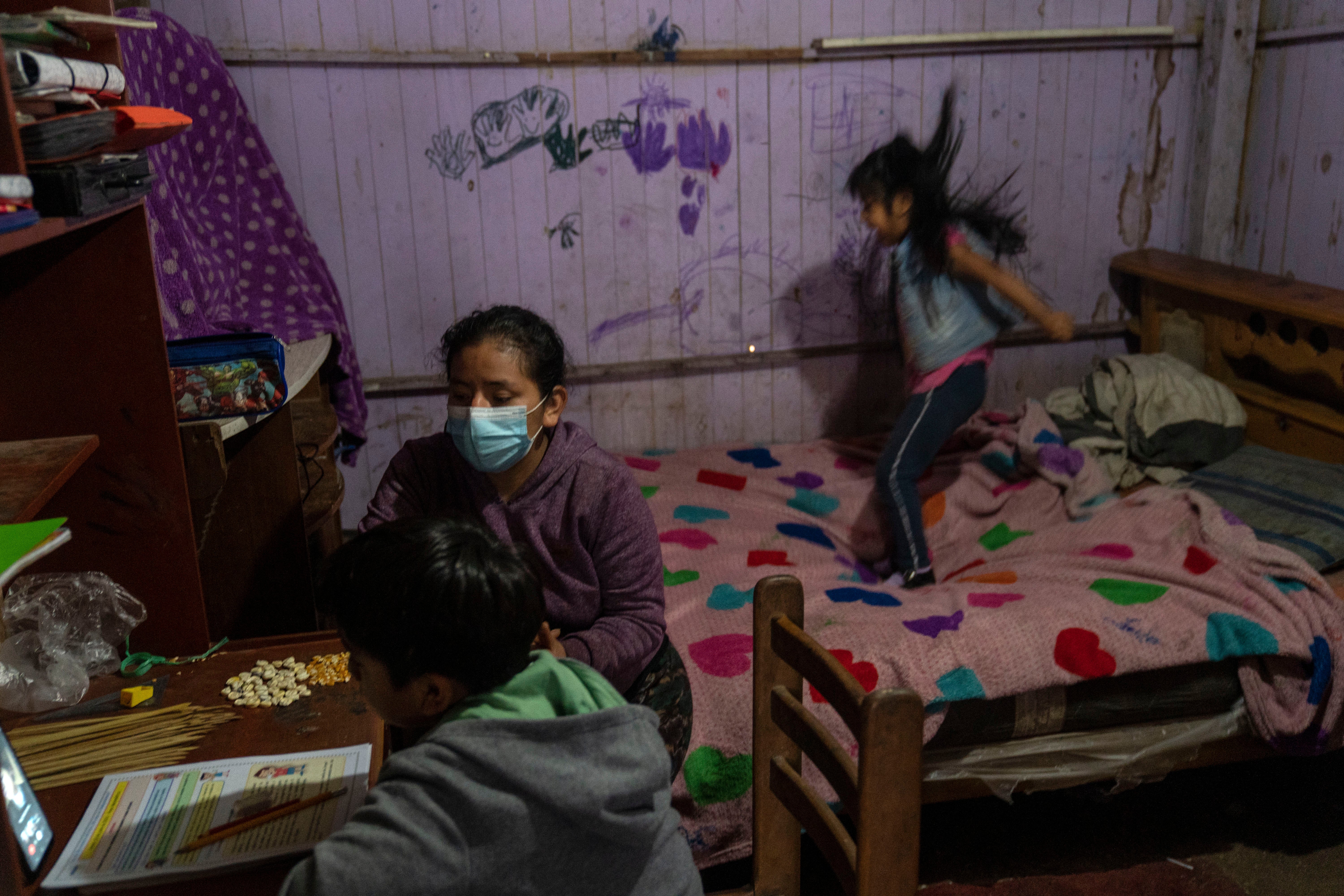 Marimar Avila sits with her son, Luis Miguel, during his virtual schooling on June 9 as her daughter, Milinka, jumps on a bed in the family’s shack in Lima’s Goshen City