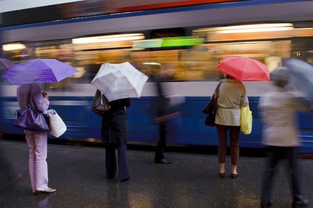 <p>Commuters wait for a tram in the rain in the centre of Zurich</p>