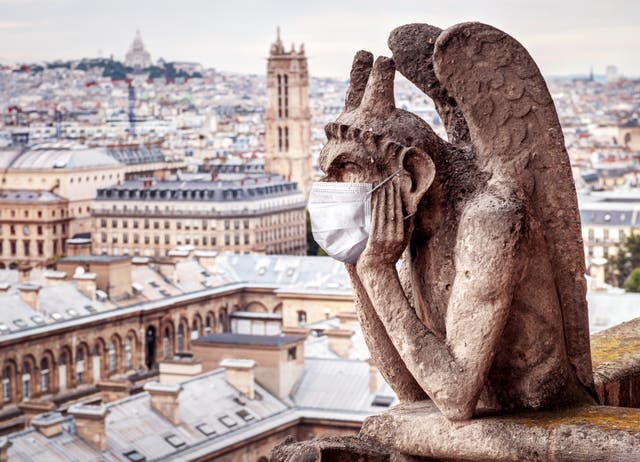 <p>A face maks adorns a gargoyle on Notre Dame in Paris, France</p>