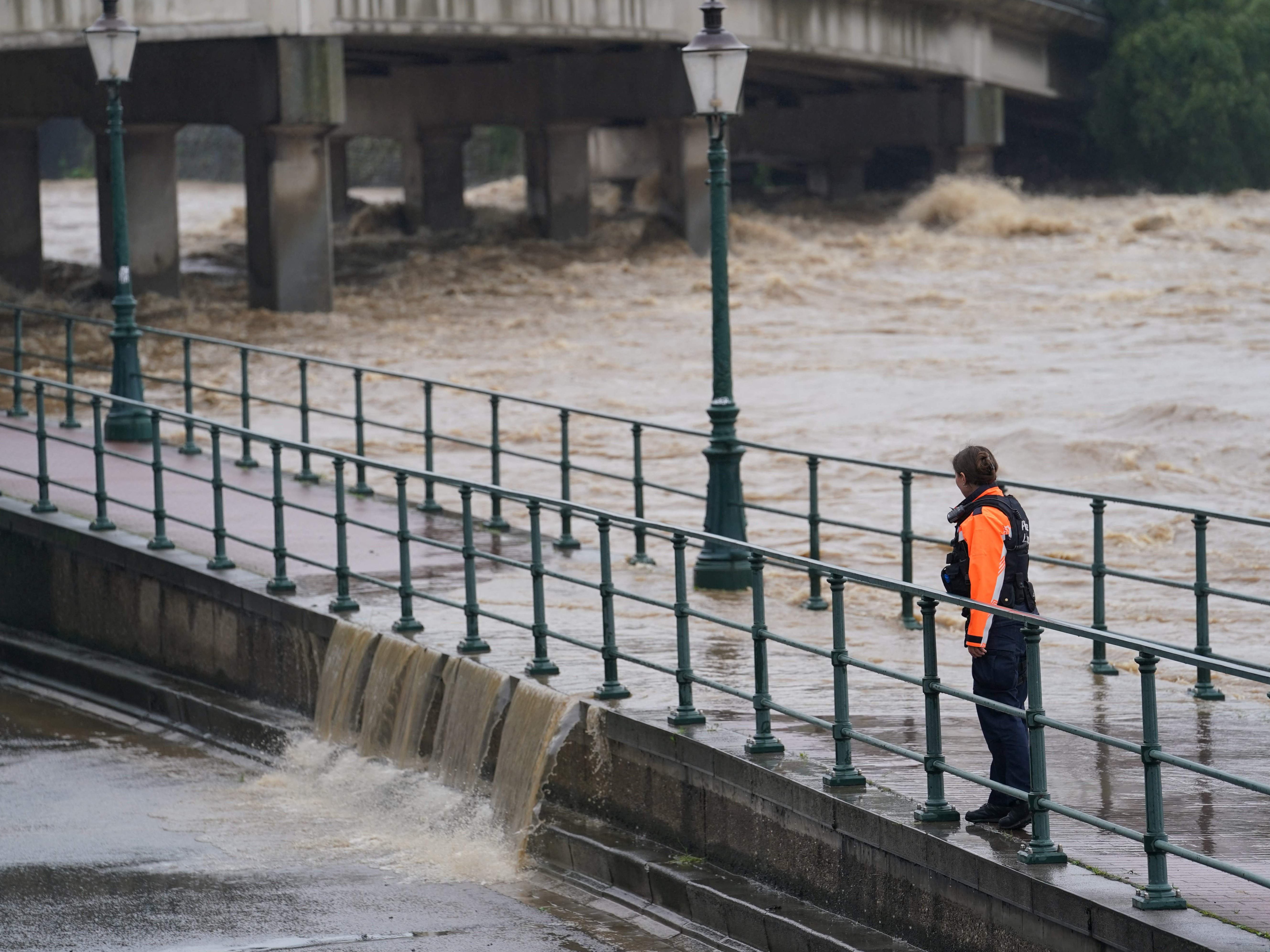 A police officer watches as water from the Meuse river breaches a barrier at the crossing with the Ourthe in Liege