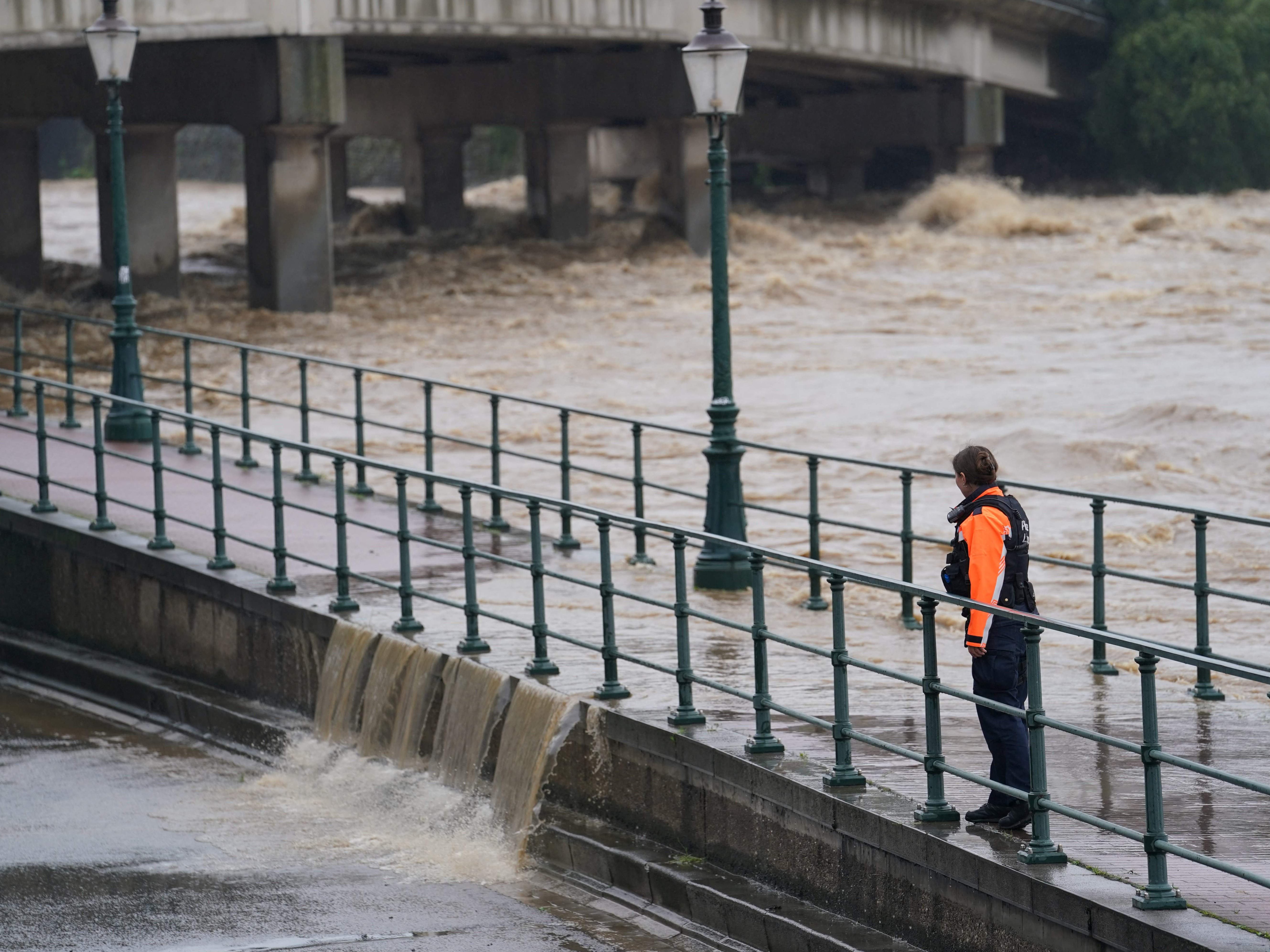 A police officer watches as water from the Meuse breaches a barrier at the crossing with the Ourthe in Liege