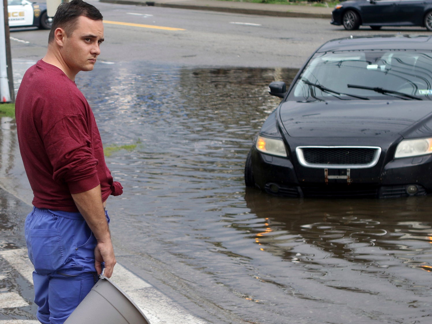 A man holds a bucket in front of his car, which stalled in floodwaters in Lodi, New Jersey