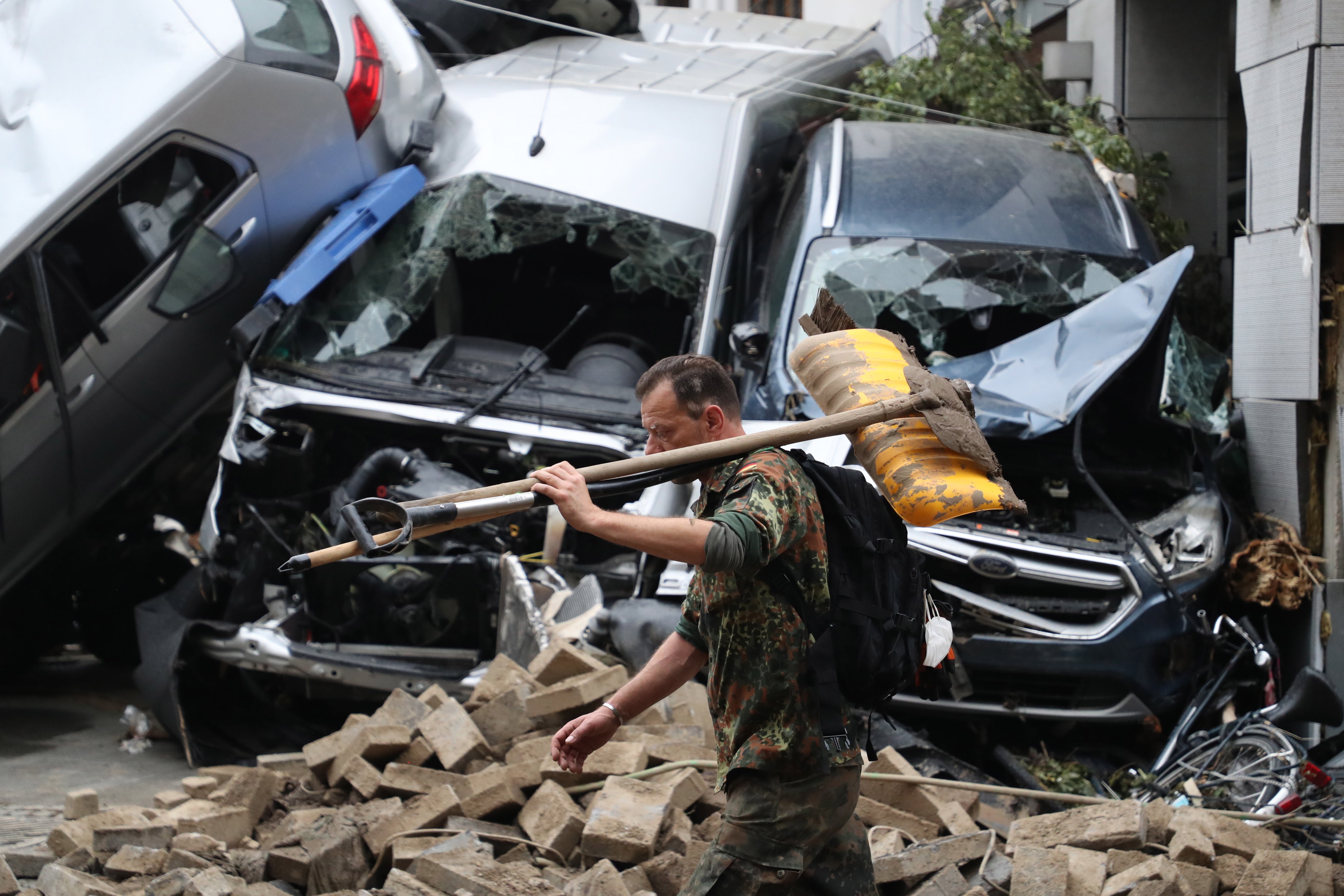 Man carrying a shovel on his shoulder walks amid the debris near damaged cars after flooding in Bad Neuenahr-Ahrweiler, Germany