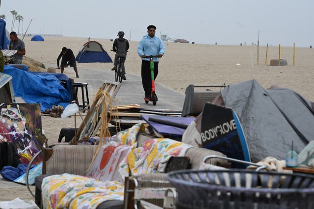 <p>A man rides a scooter past tents as authorities prepare to begin clearing homeless encampments at the Venice Beach Boardwalk on July 2, 2021 in Los Angeles</p>