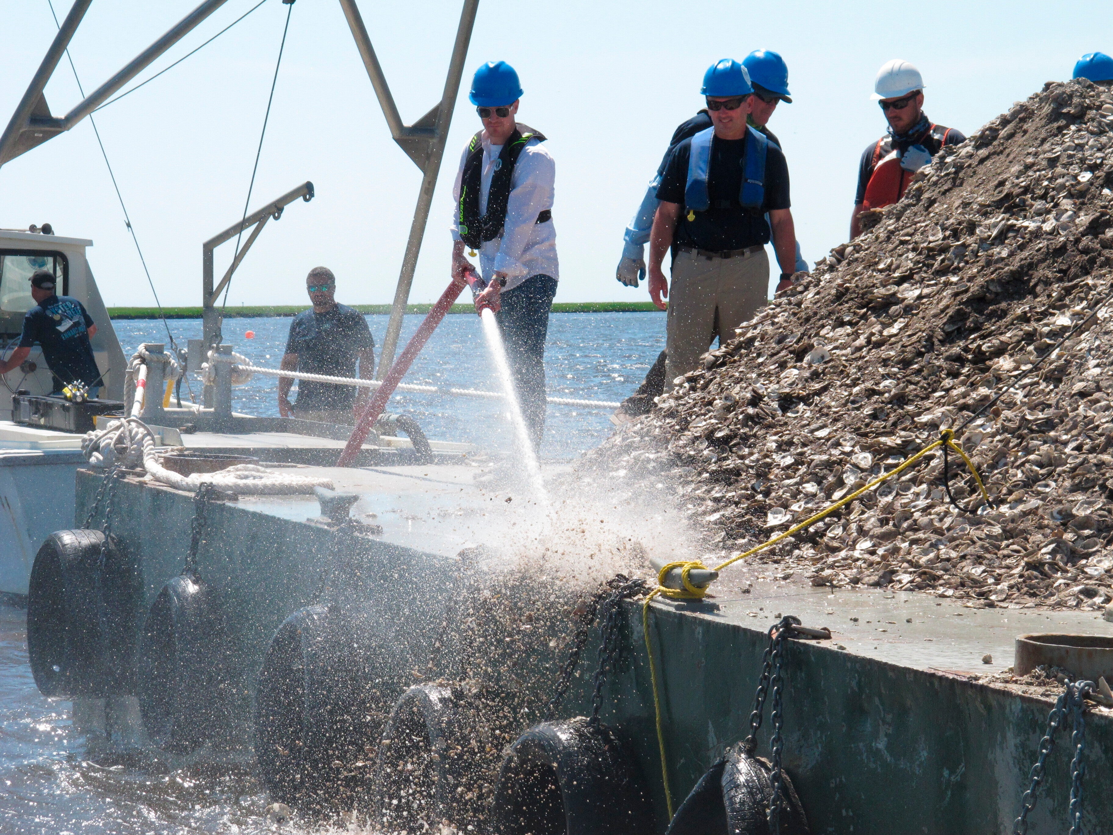 File New Jersey Environental Protection Commissioner Shawn LaTourette, left, uses a high-pressure hose to blast clam and oyster shells from a barge into the Mullica River in Port Republic