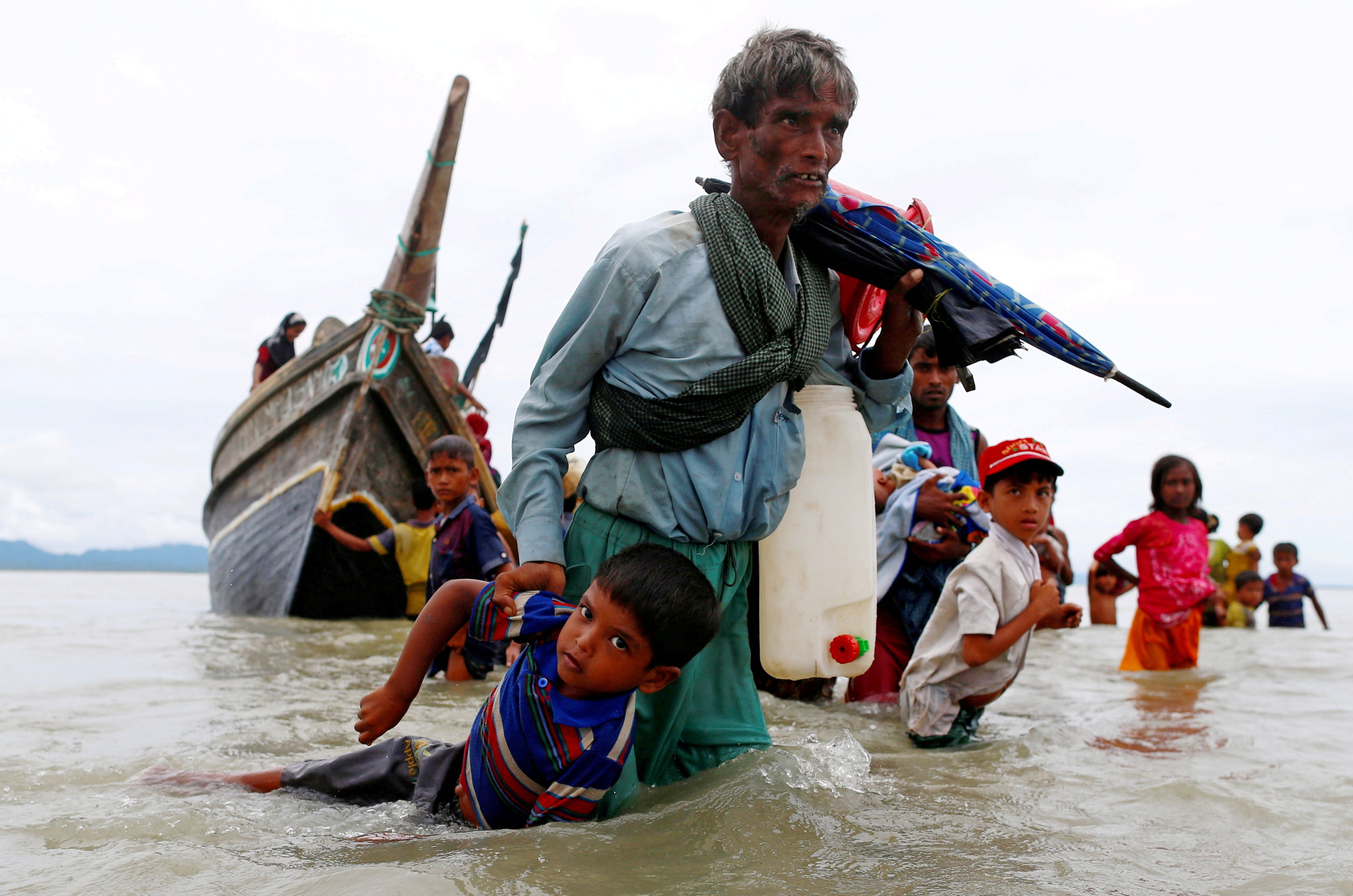A Rohingya refugee pulls a child as they walk to the shore after crossing the Bangladesh-Myanmar border by boat through the Bay of Bengal in Shah Porir Dwip in 2017