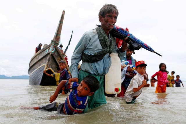 <p>A Rohingya refugee pulls a child as they walk to the shore after crossing the Bangladesh-Myanmar border by boat through the Bay of Bengal in Shah Porir Dwip in 2017</p>