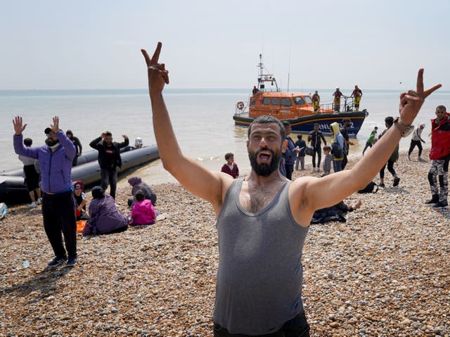 <p>Migrants make their way up the beach after arriving on a small boat at Dungeness in Kent</p>