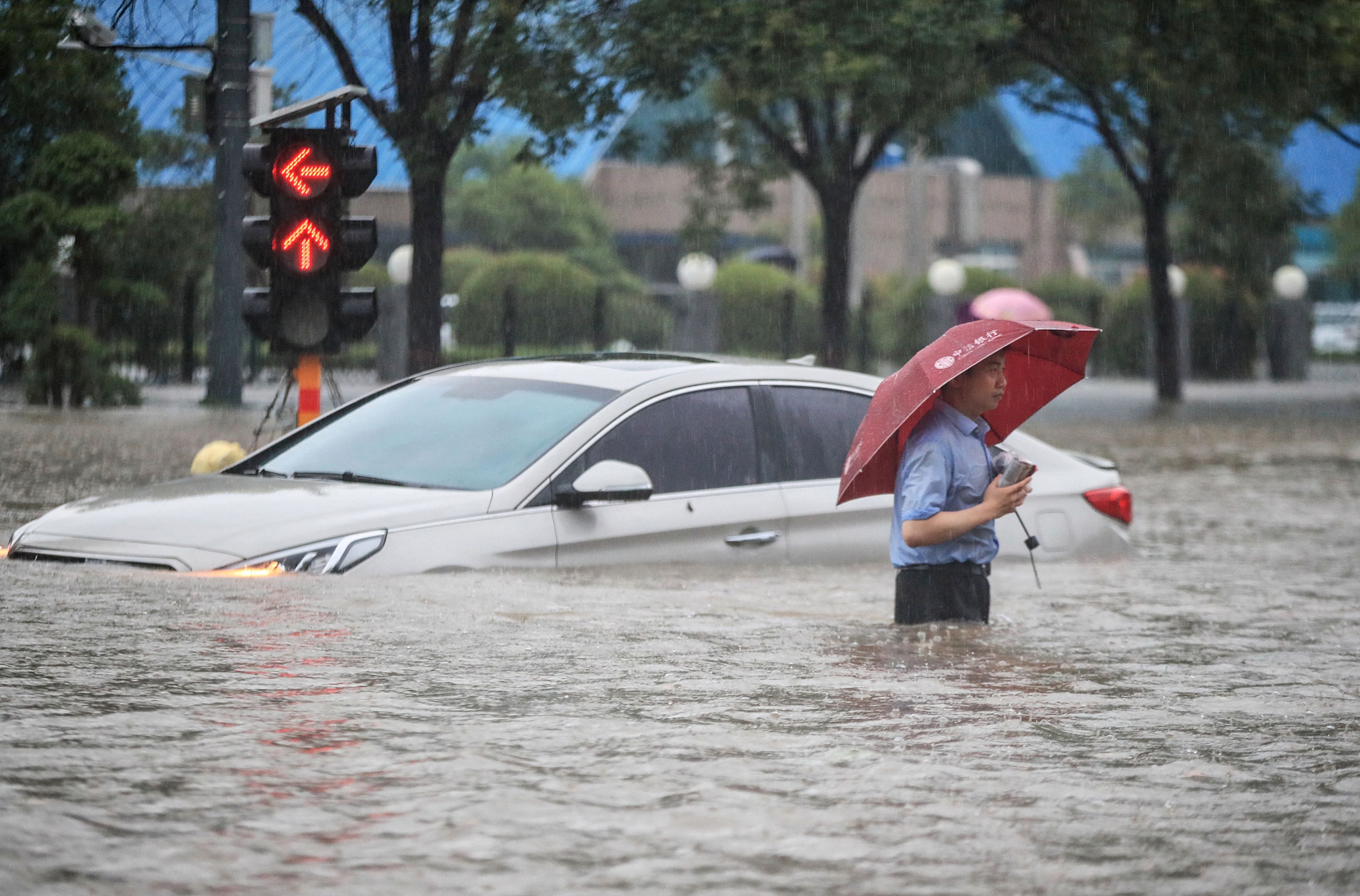 <p>A man wades past a submerged car along a flooded street following heavy rains in Zhengzhou on Tuesday</p>