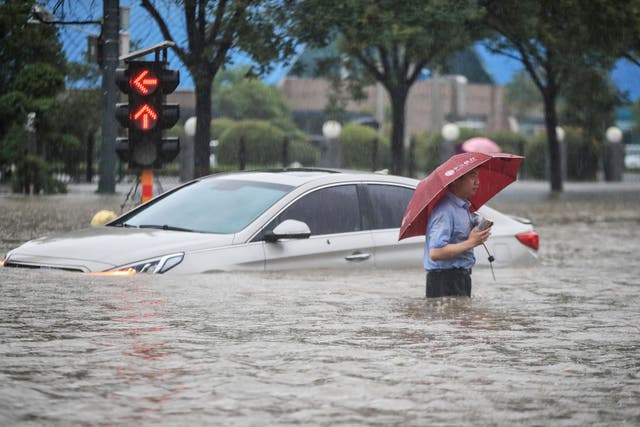 <p>Un hombre pasa junto a un automóvil sumergido a lo largo de una calle inundada luego de las fuertes lluvias en Zhengzhou el martes.</p>