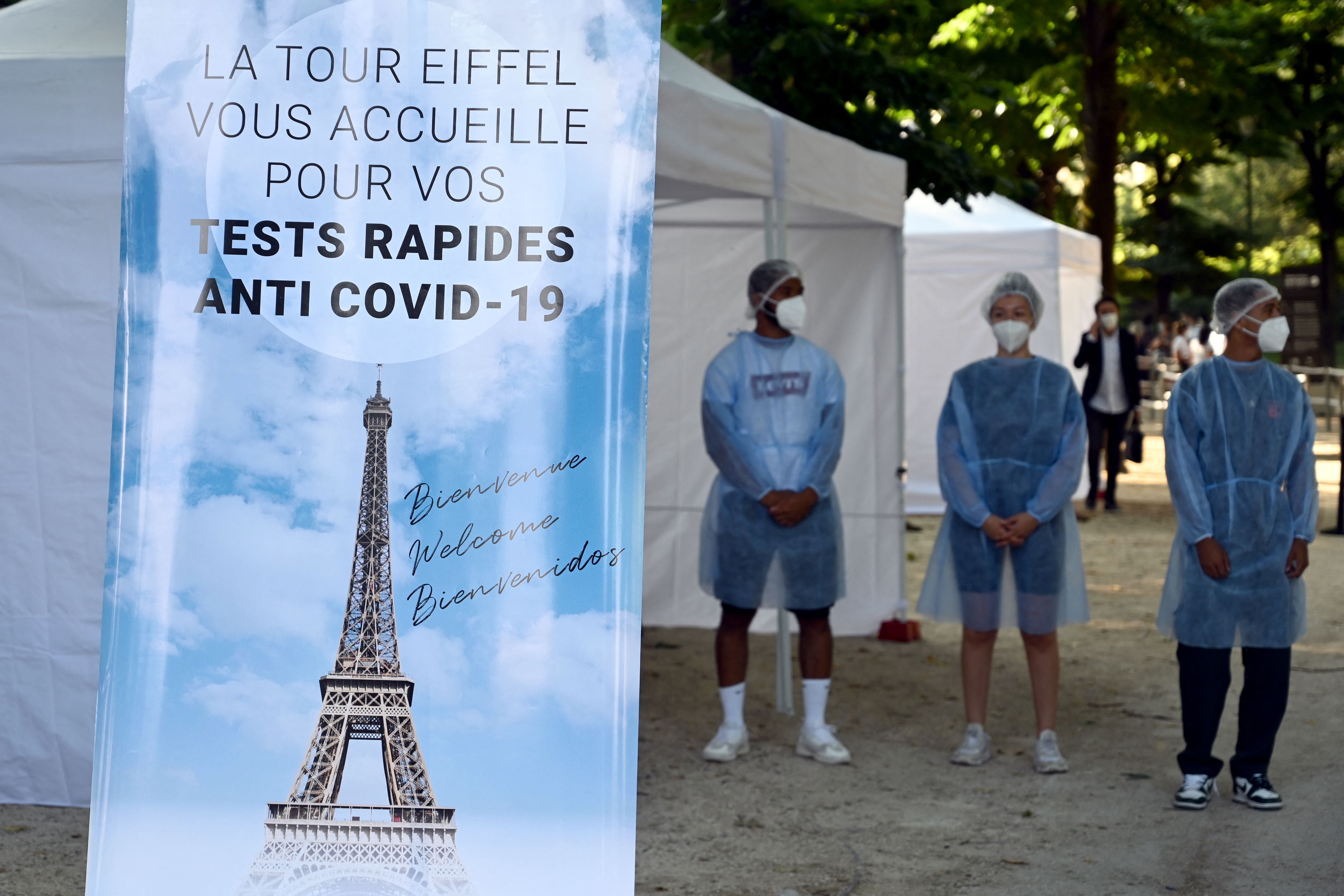 Health workers stands near a Covid-19 antigenic tests area, as a banner reads 'The Eiffel Tower welcomes you for your anti Covid-19 quick tests'