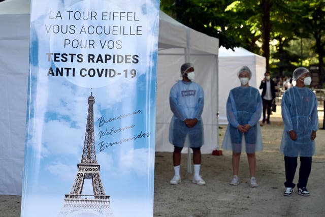 <p>Health workers stands near a Covid-19 antigenic tests area, as a banner reads 'The Eiffel Tower welcomes you for your anti Covid-19 quick tests'</p>