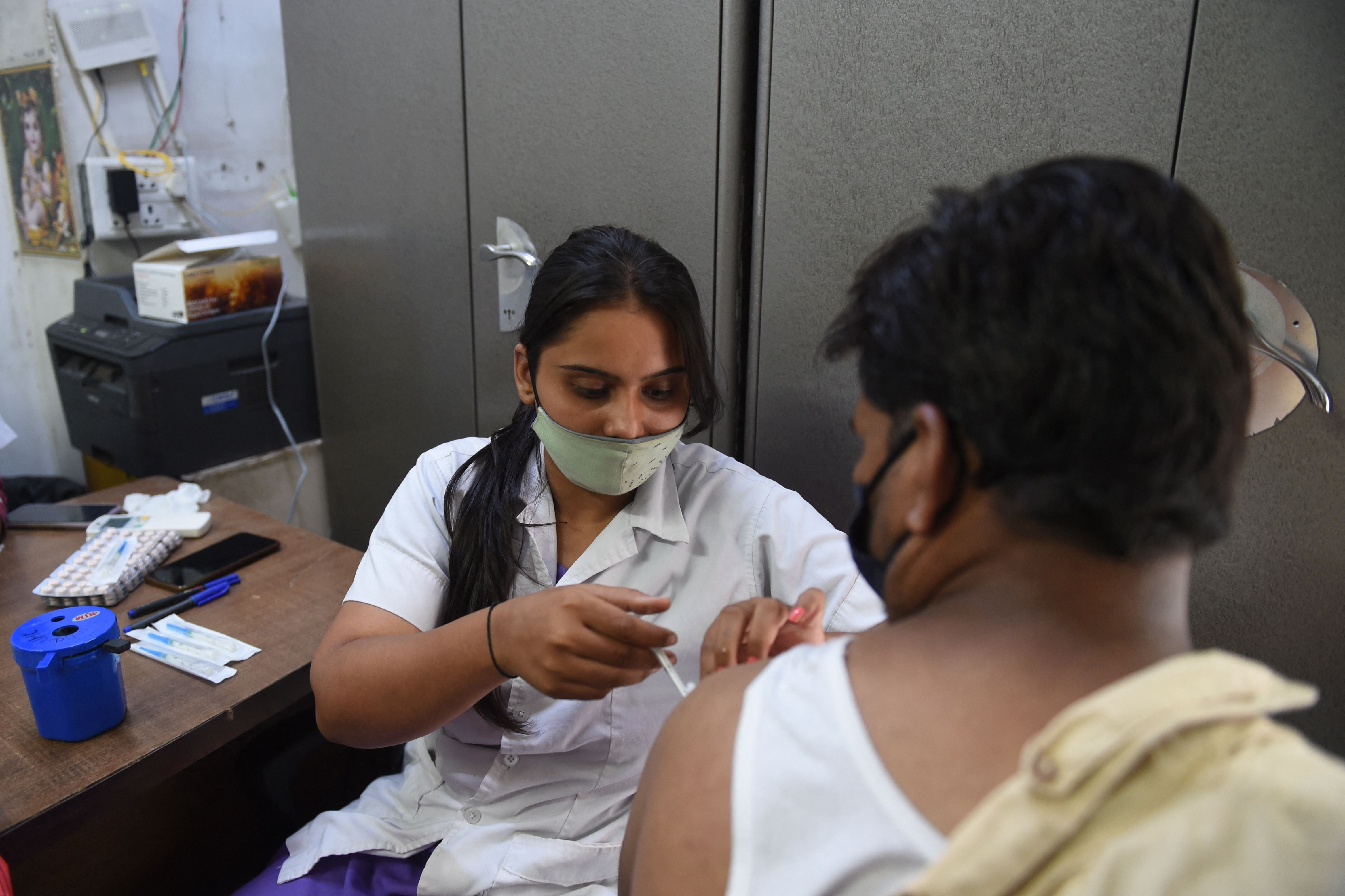 A health worker (L) inoculates a man with a dose of the Covishield vaccine against the Covid-19 coronavirus during a vaccination drive for shopkeepers and their staff members in Ahmedabad