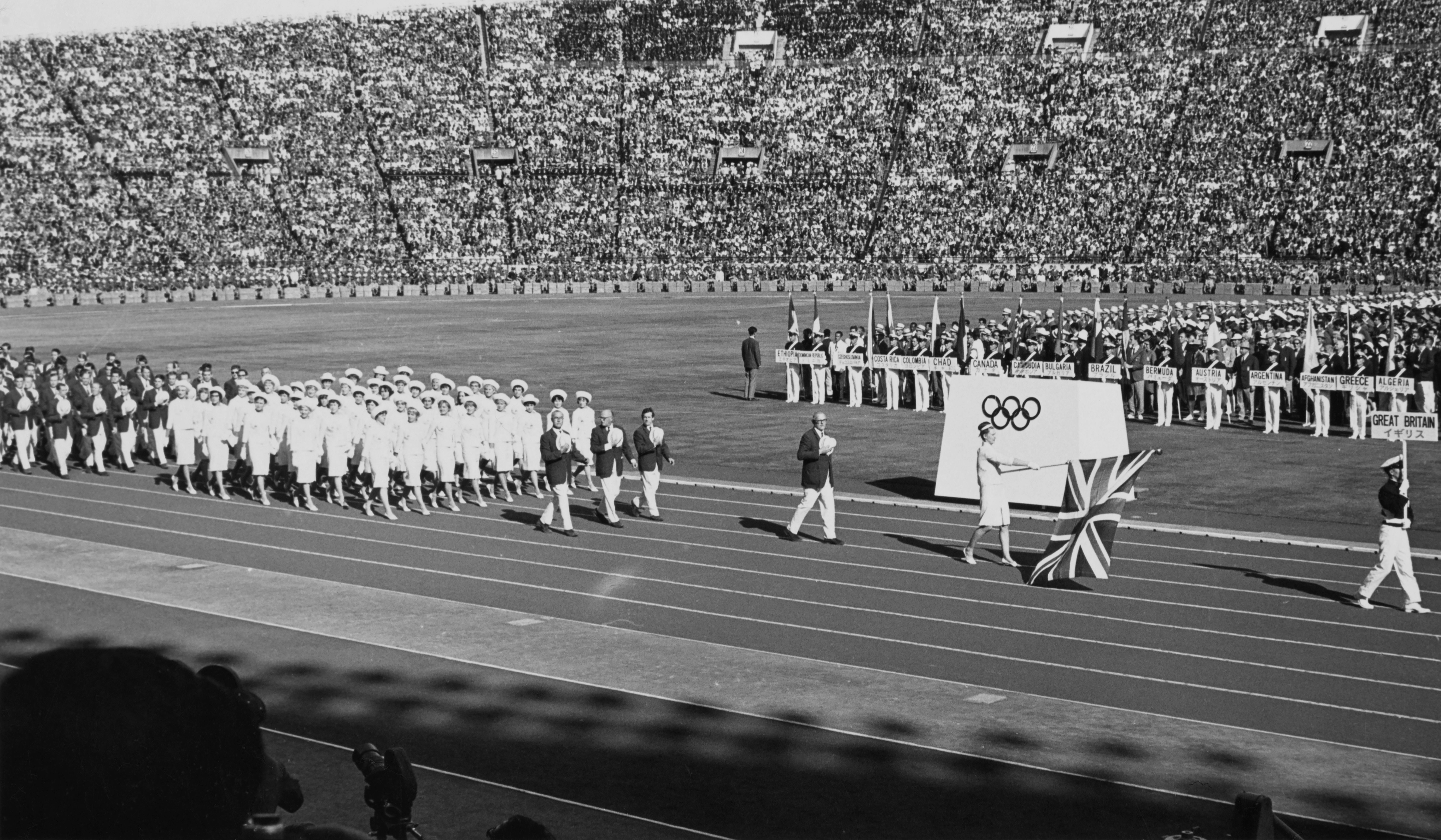 Swimming gold medalist Anita Lonsbrough of Great Britain carries the Union flag ahead of the Great Britain team during the opening ceremony at the National Stadium for the Summer Olympic Games on 10 October 1964 at the National Stadium in Kasumigaoka, Shinjuku, Tokyo, Japan