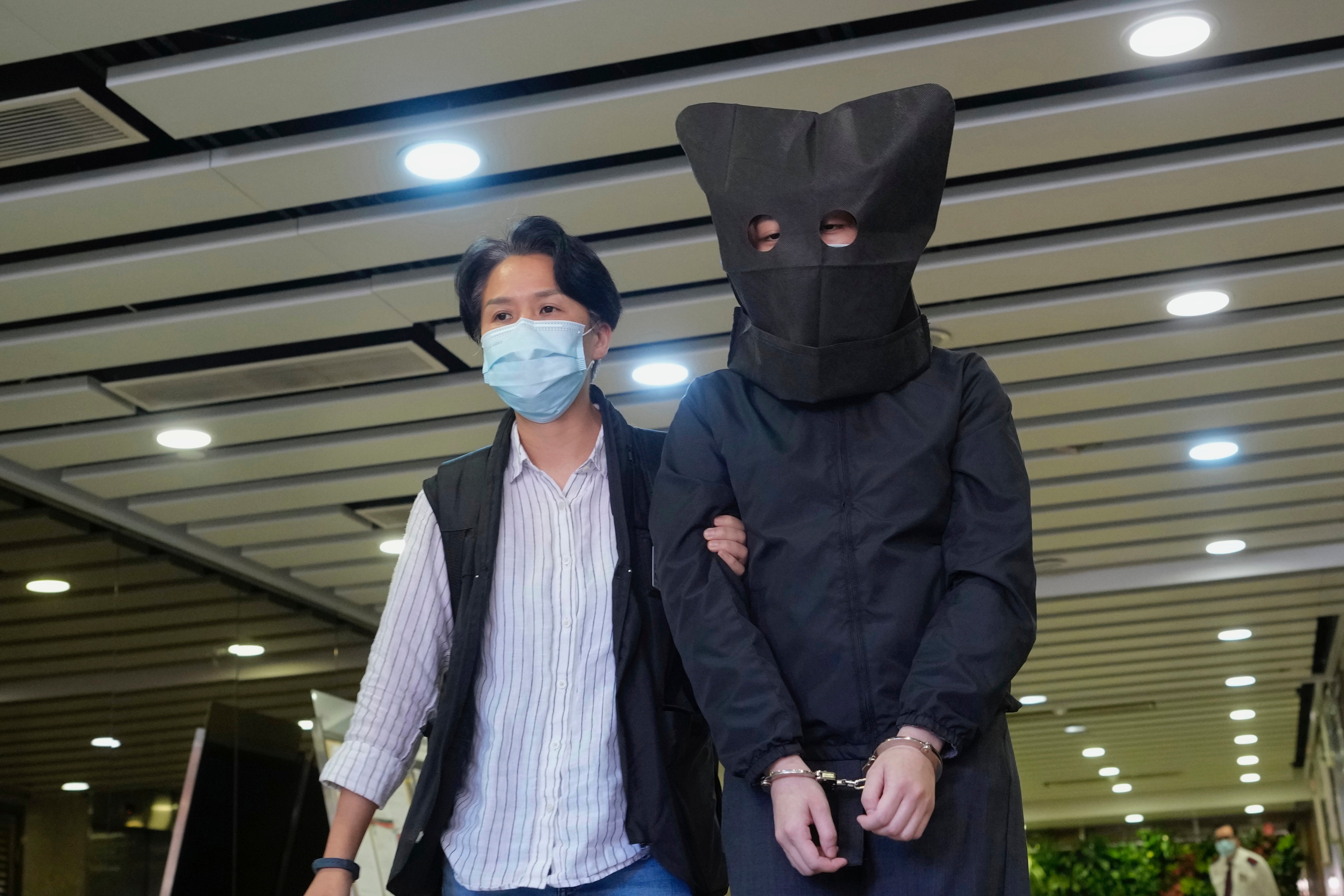 A hooded suspect is accompanied by a police officer in Hong Kong in the latest arrests made amid a crackdown on dissent in the city