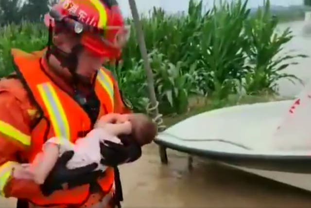 <p>Screengrab: A Chinese firefighter is seen holding a rescued baby while wading through floodwater</p>