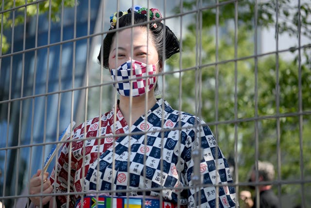 <p>A woman in traditional clothing looks on from behind a fence prior to the Opening Ceremony of the Tokyo 2020 Olympic Games at Olympic Stadium</p>