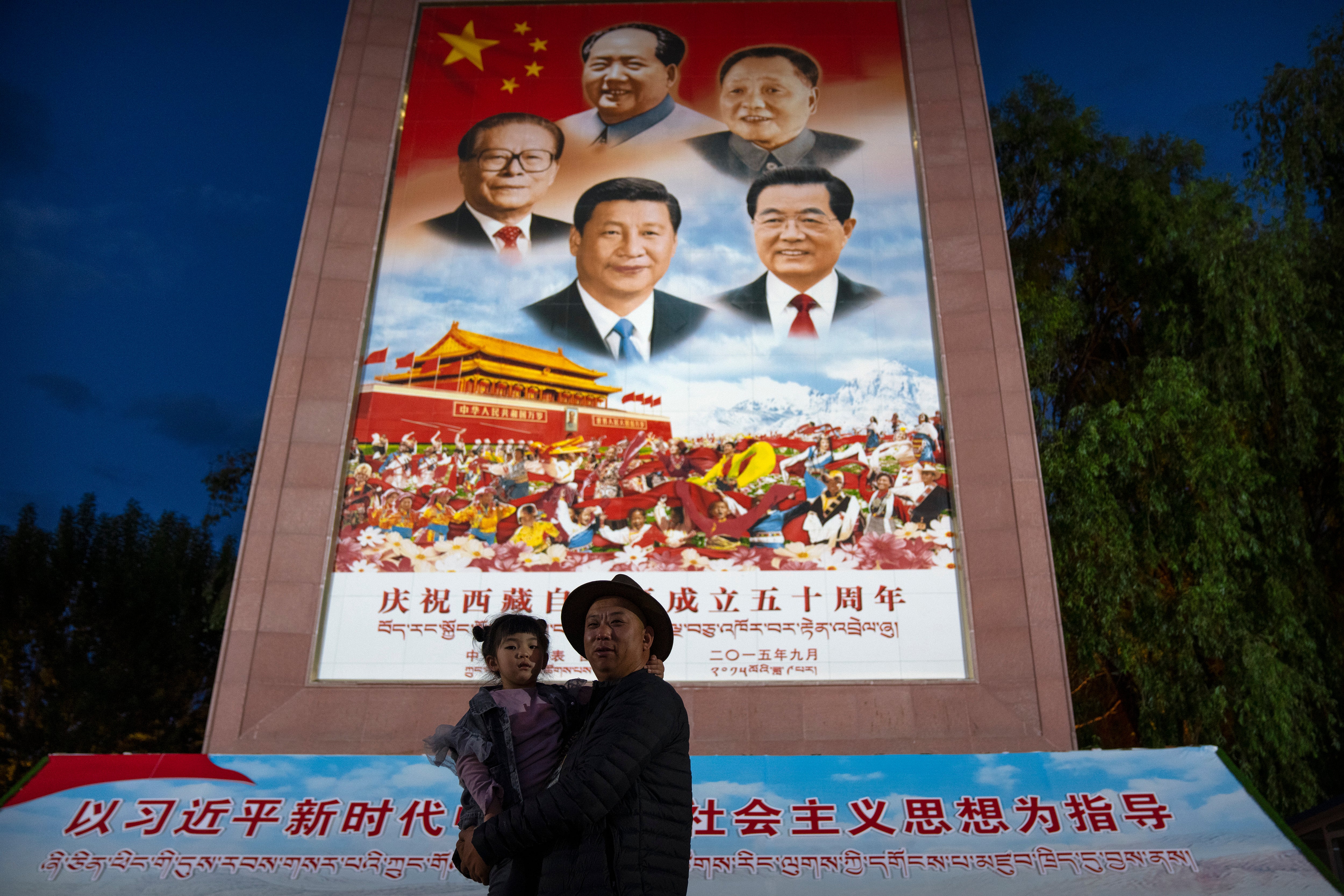 File image: A man holds a girl as they pose for a photo in front of a large mural depicting Chinese President Xi Jinping, bottom centre, and other Chinese leaders at a public square at the base of the Potala Palace in Lhasa in western China's Tibet Autonomous Region on 1 June, 2021.