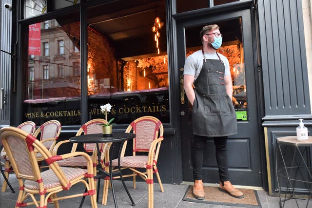A bartender wearing a face mask stands outside a bar in Cardiff (PA)