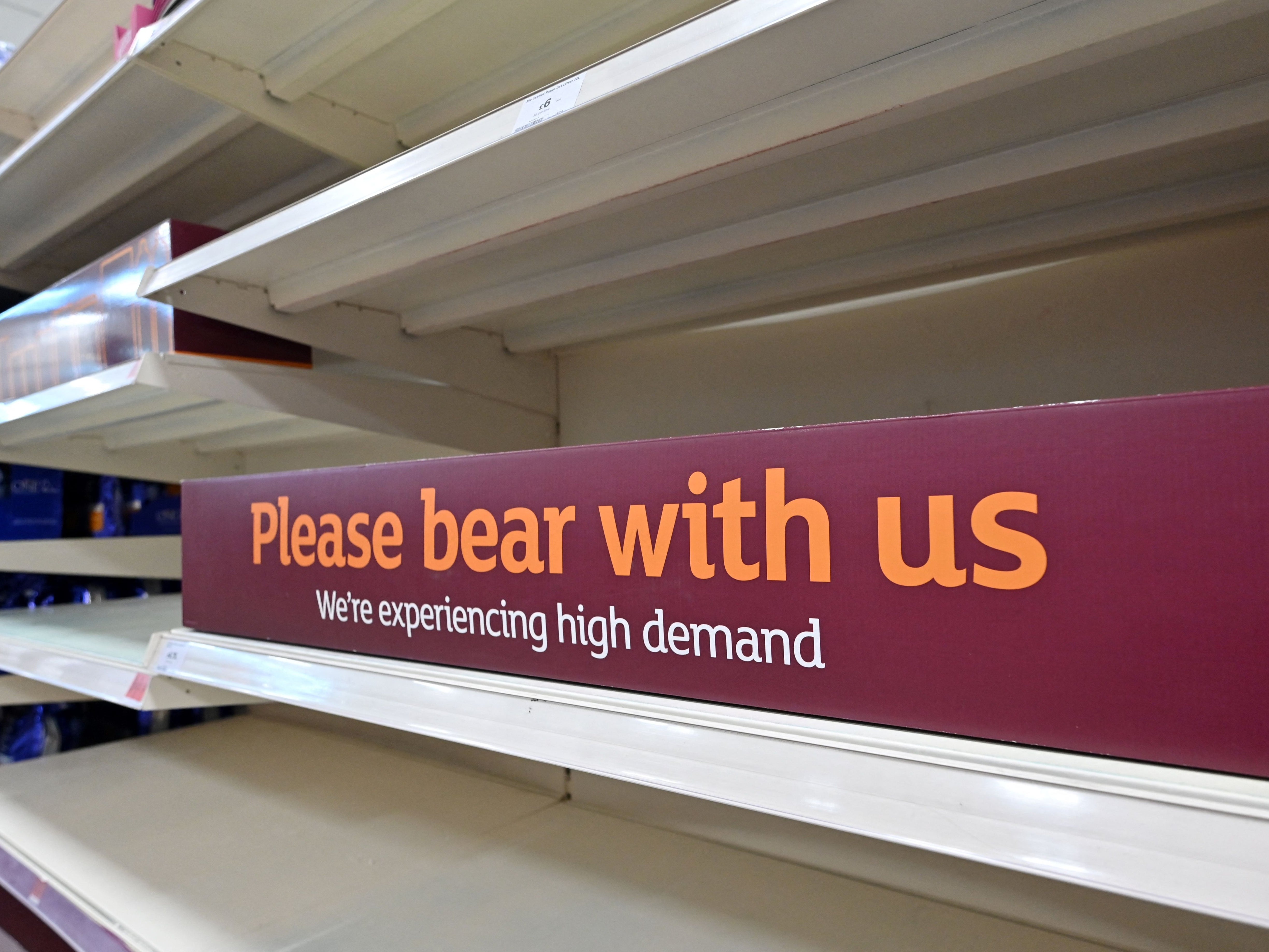 A sign requesting shoppers' patience about products temporarily out of stock is displayed on empty shelves
