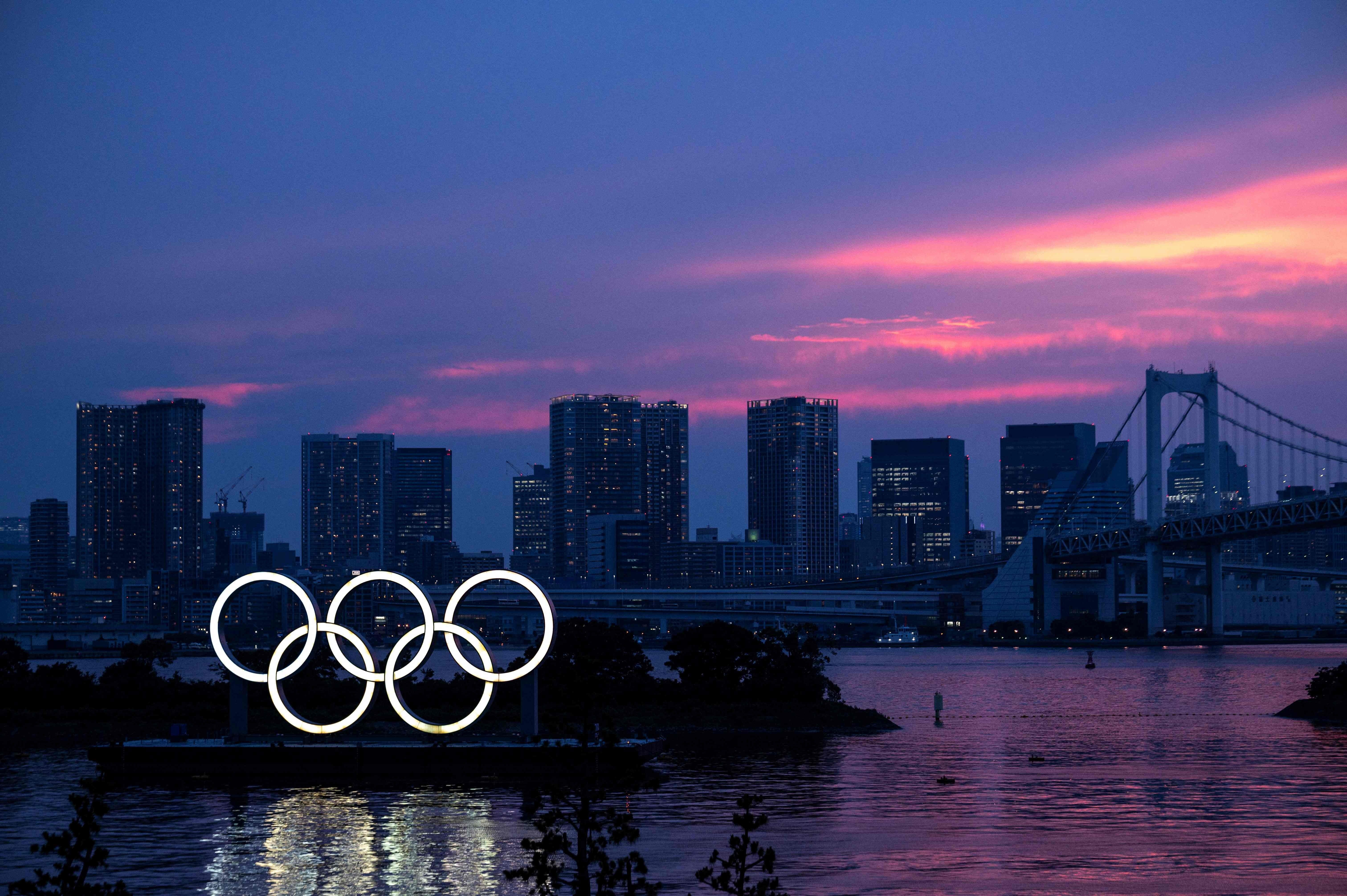 A general view shows the Olympic rings lit up at dusk, with the Rainbow bridge in the background, on the Odaiba waterfront in Tokyo