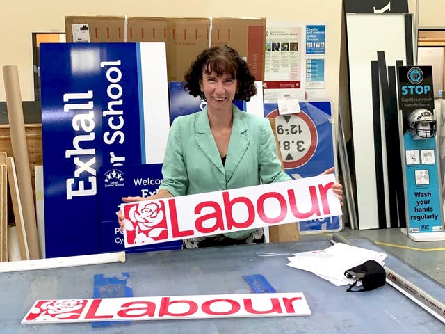 <p>Anneliese Dodds, a white woman with curly brown hair, smiles in a signage factory, hoping a red Labour sign.</p>