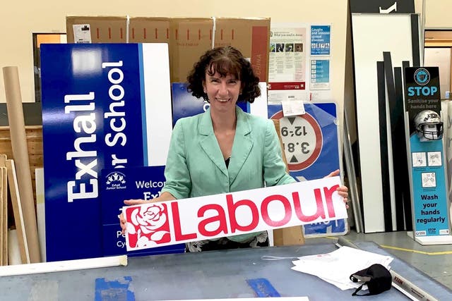 <p>Anneliese Dodds, a white woman with curly brown hair, smiles in a signage factory, hoping a red Labour sign.</p>