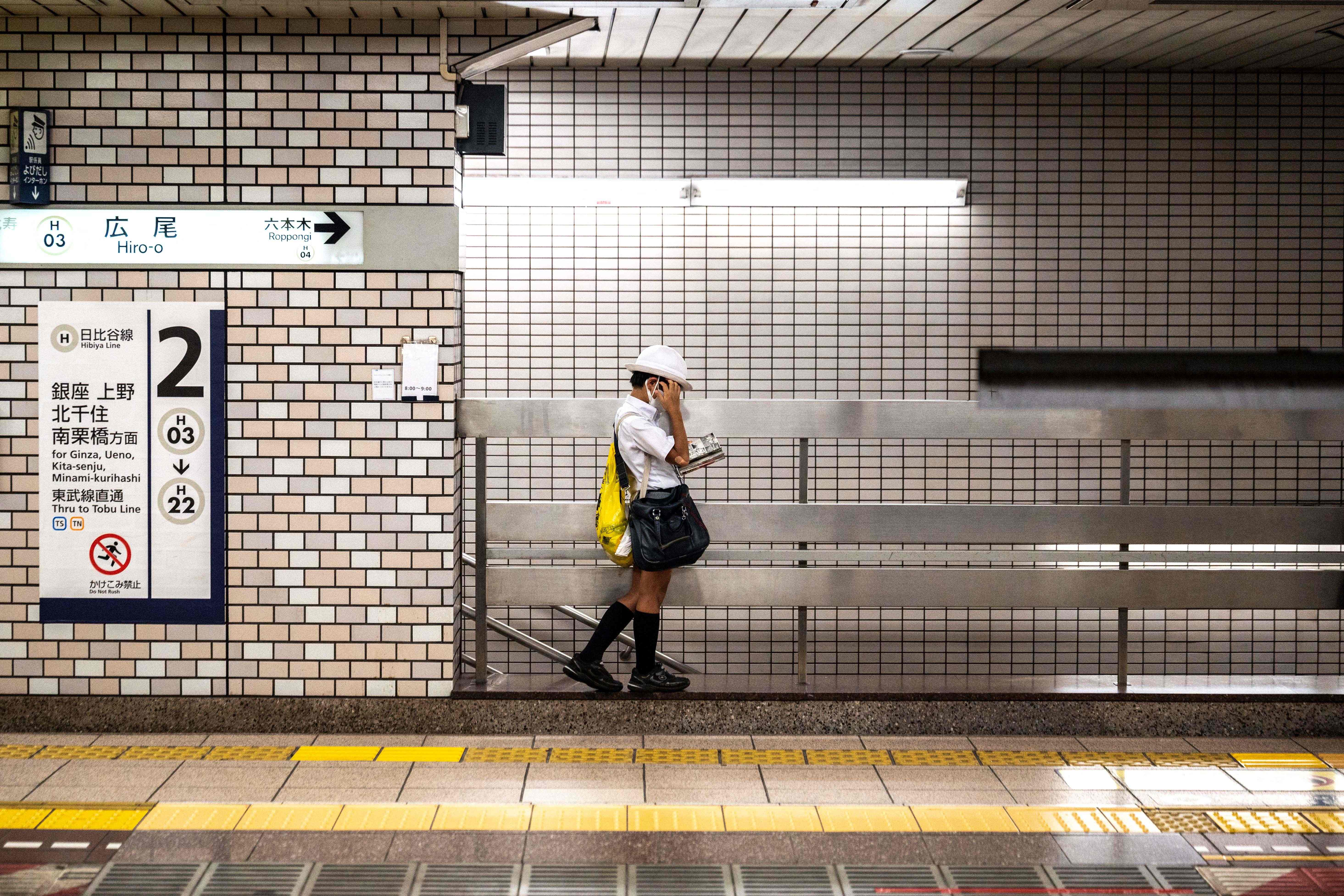 A schoolboy reads a manga comic book while waiting for the train on a platform in Tokyo