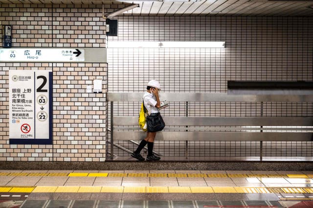 <p>A schoolboy reads a manga comic book while waiting for the train on a platform in Tokyo</p>